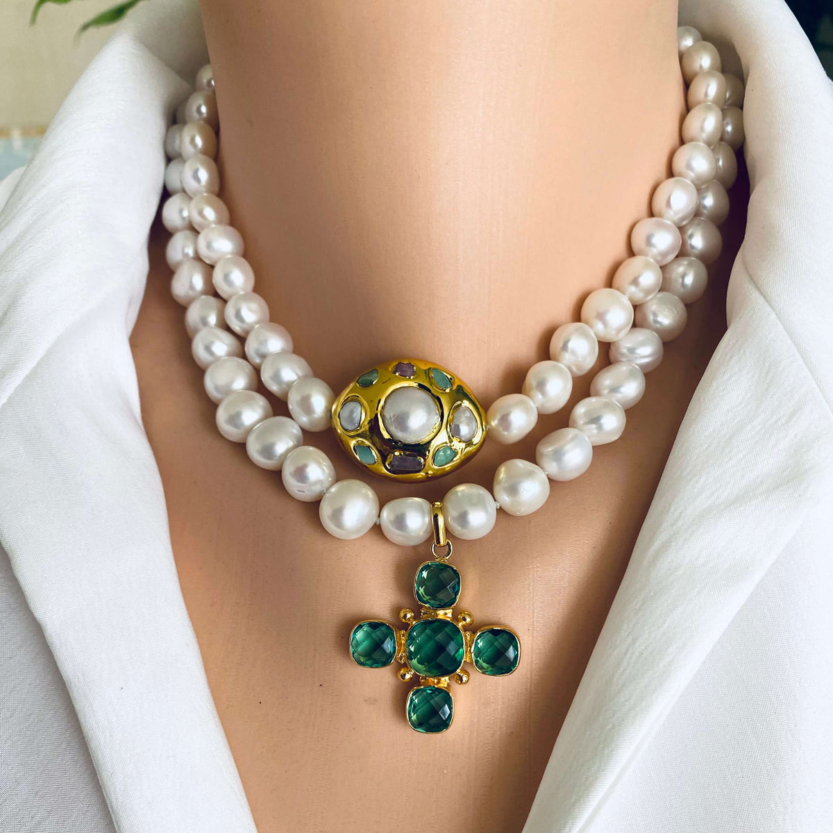 White pearl necklace with gold accent featuring a gold focal point and emerald green gemstones.