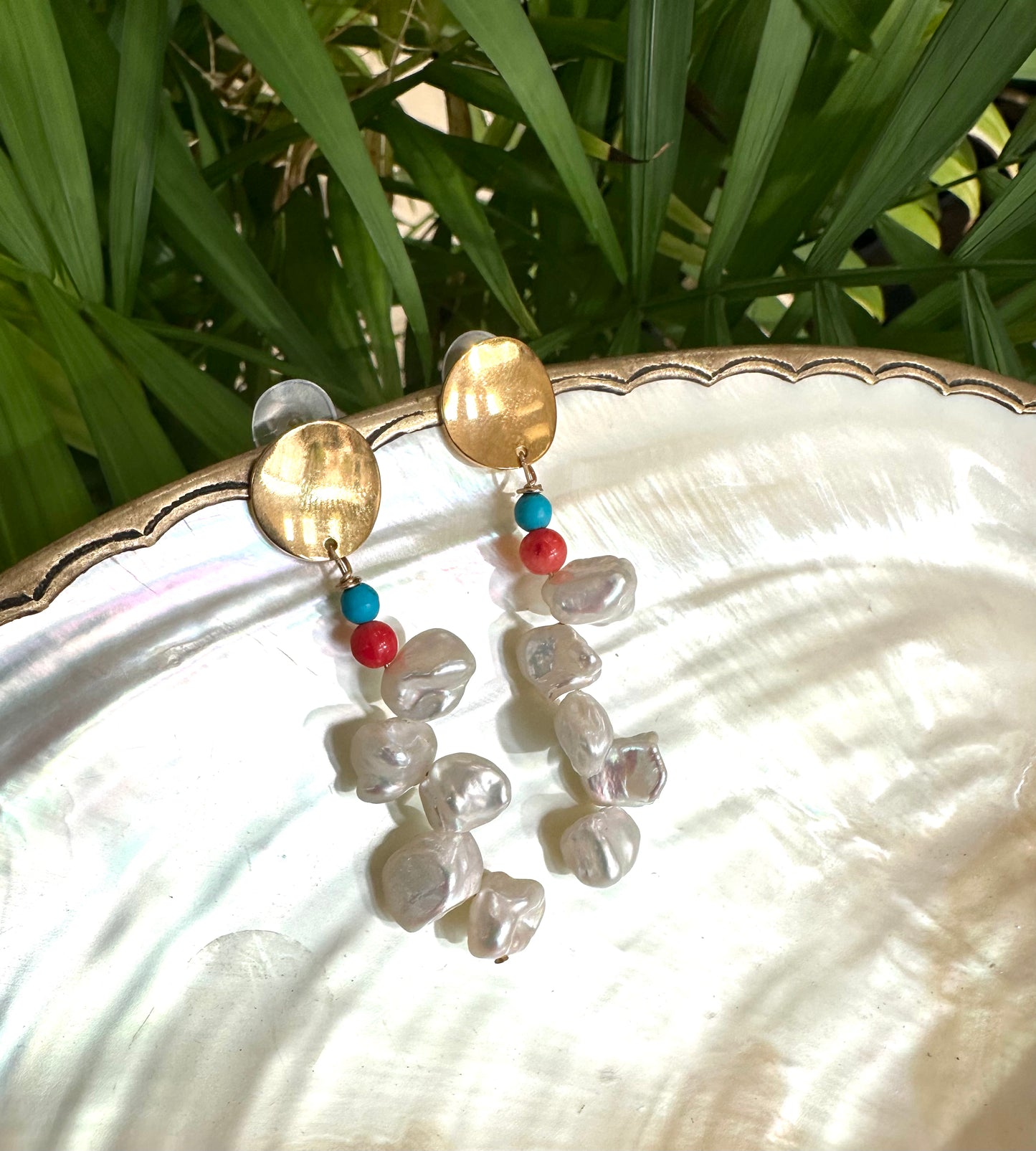 Baroque Keshi Pearl Earrings hanging from a white pearl shell with green leaves in background, gold-filled dangle design