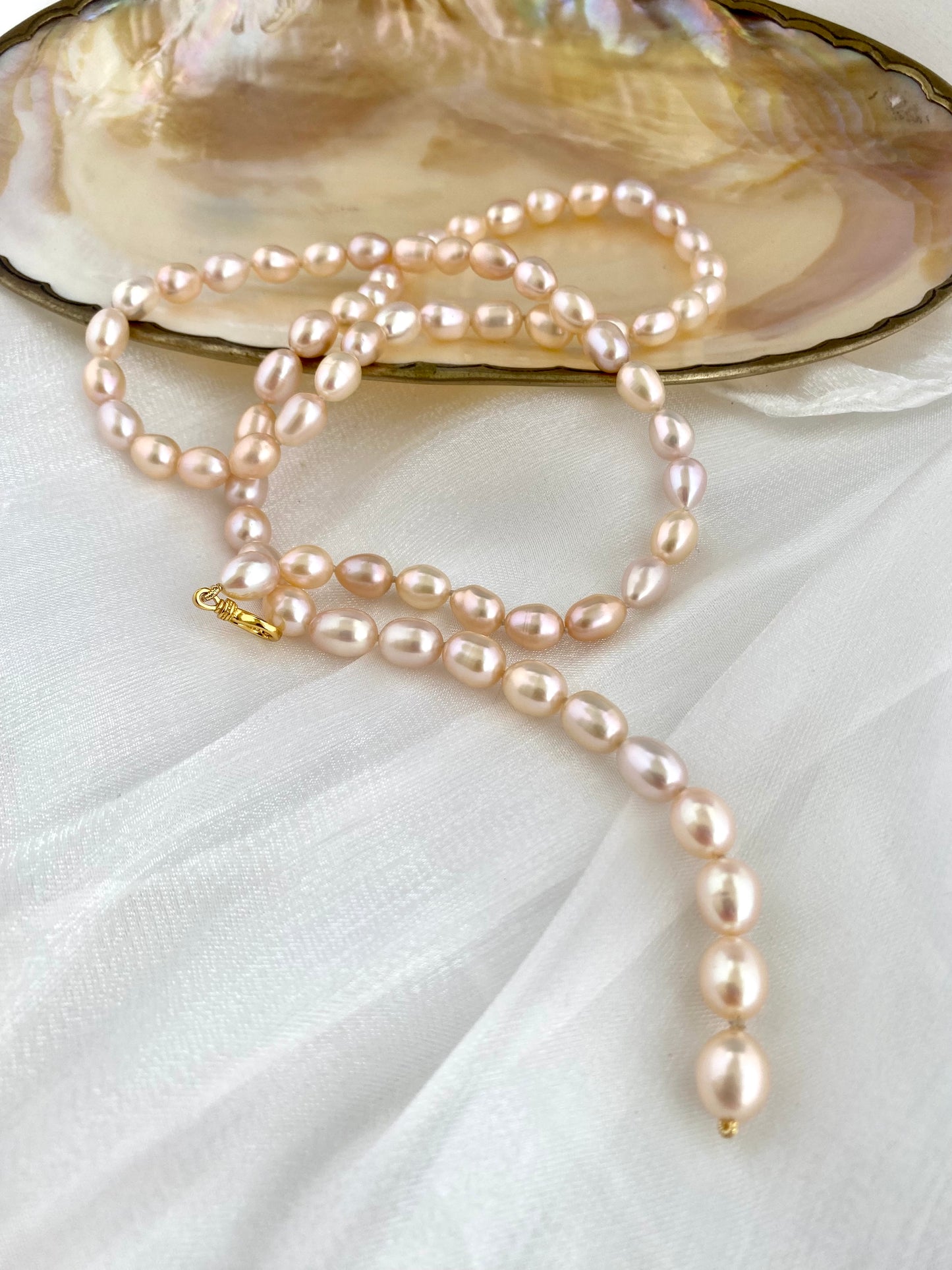Pearl necklace draped over an open shell on a white fabric background