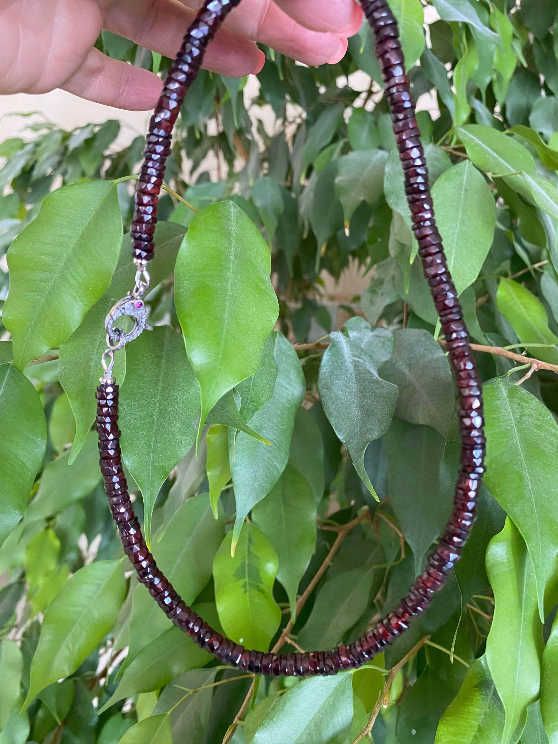 Garnet beaded necklace with diamond & ruby pavé clasp displayed against green leaves.
