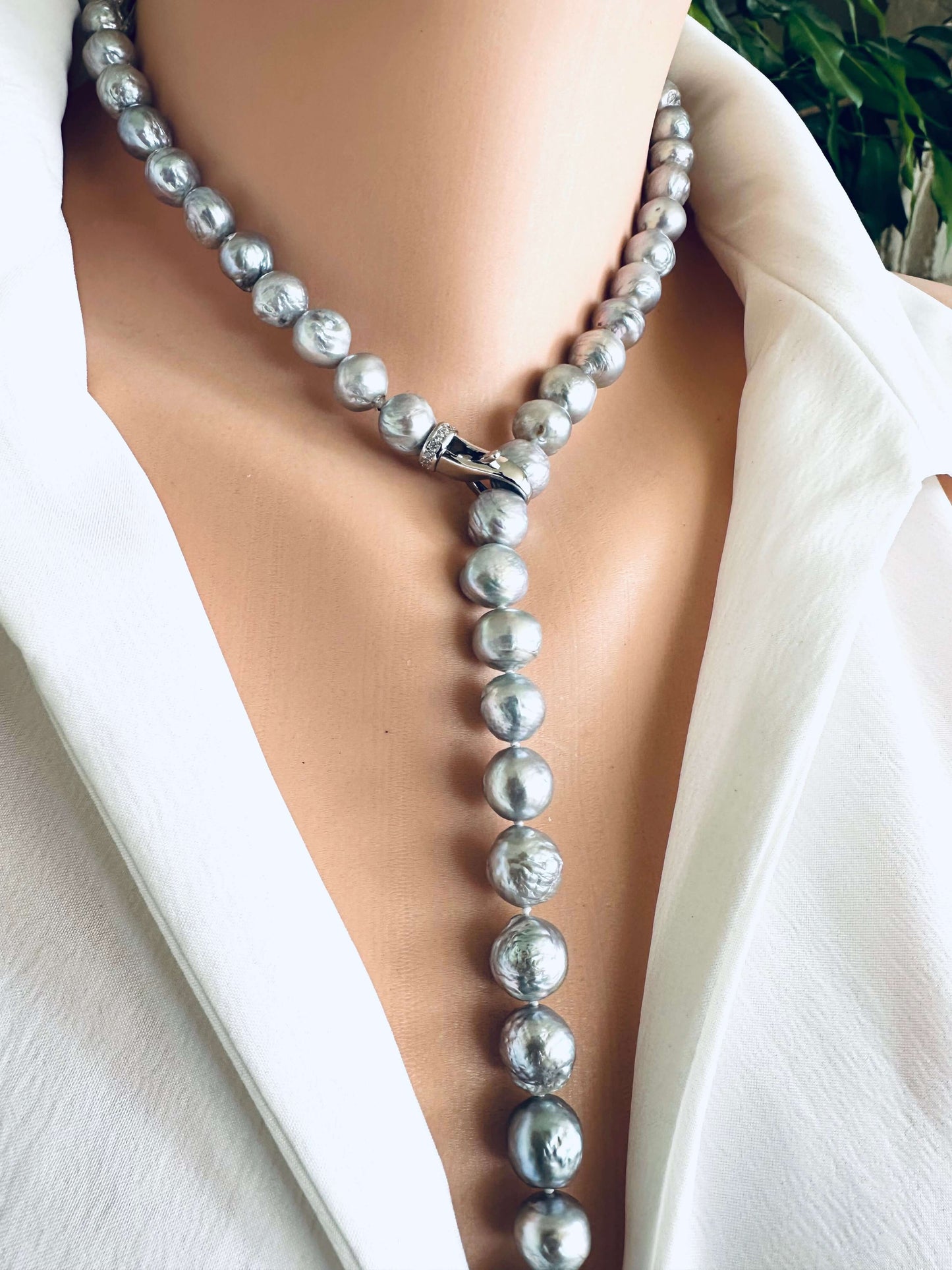 Pearl necklace draped over a white garment with a blurred green plant background