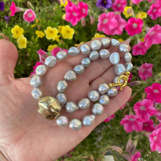 Grey pearl necklace with gold marine clasp held in hand showing hand-knotted freshwater pearls