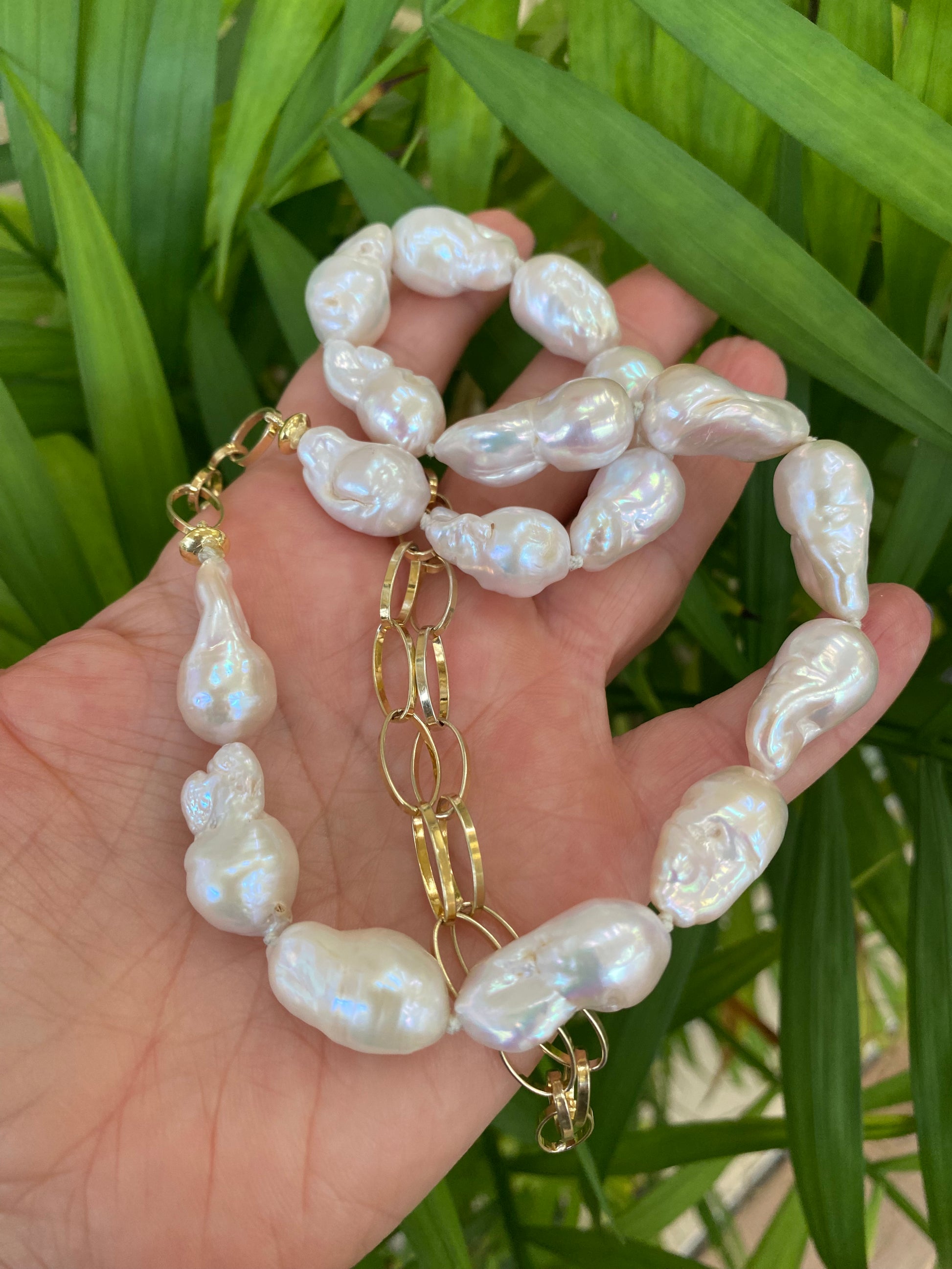 Handcrafted baroque pearl gold chain necklace photographed outdoors with leafy green background — natural light lifestyle jewelry photo by Loulia Pearl Jewelry