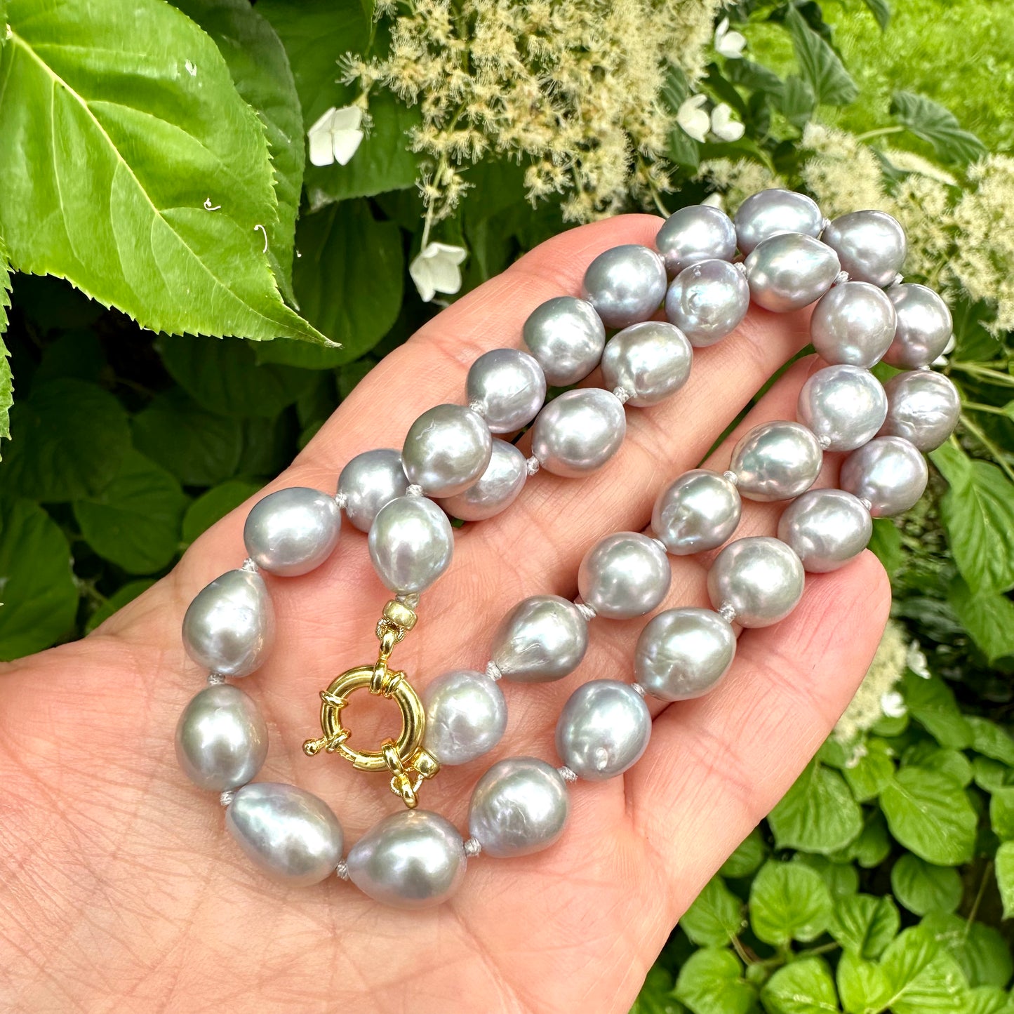 Grey Pearl Necklace held in hand against summer foliage – outdoor detail shot
