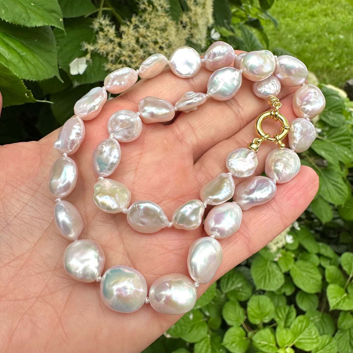 Close-up of coin pearl necklace held in hand against summer foliage