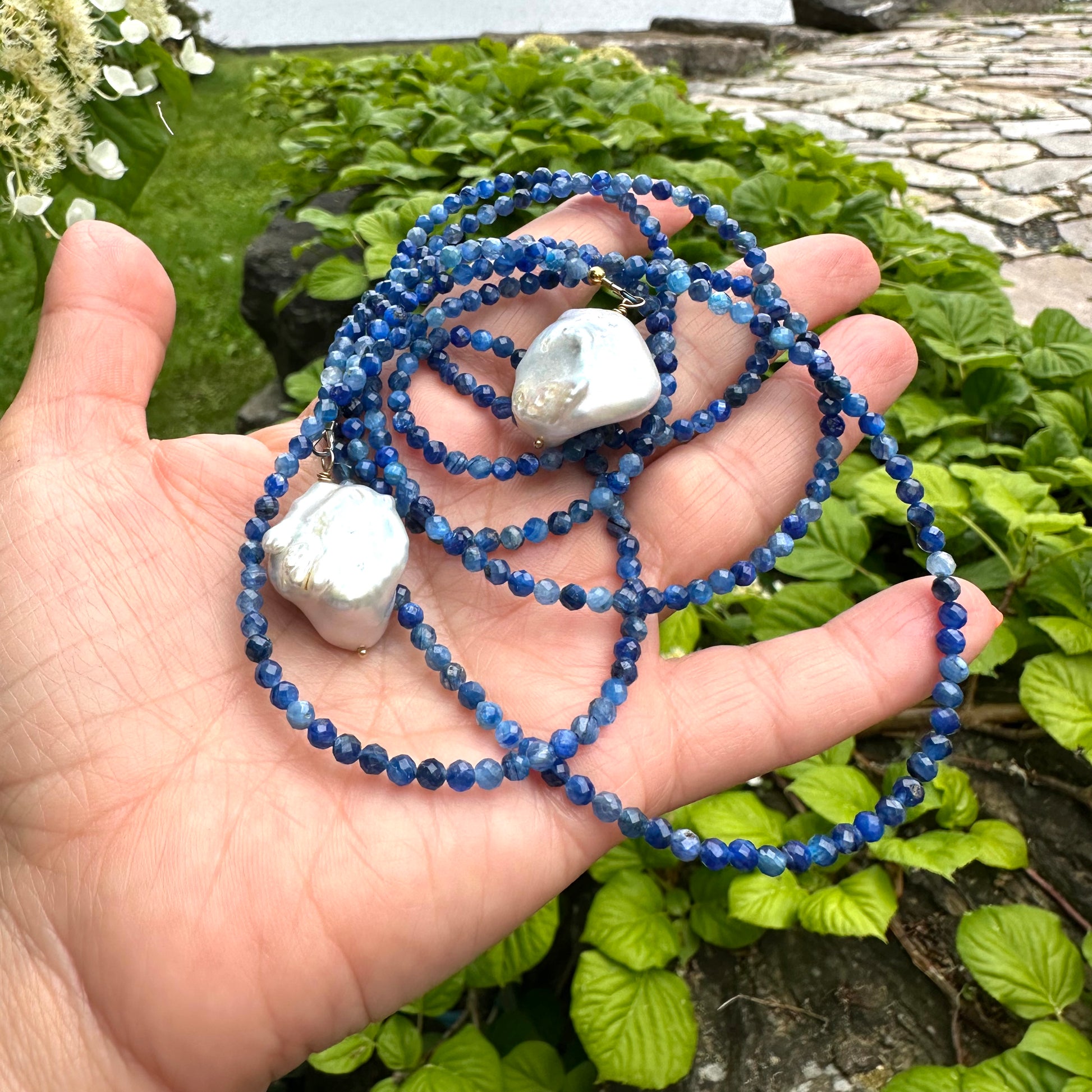 Kyanite and baroque pearl lariat necklace held in hand, featuring denim-blue kyanite beads and large baroque pearls.