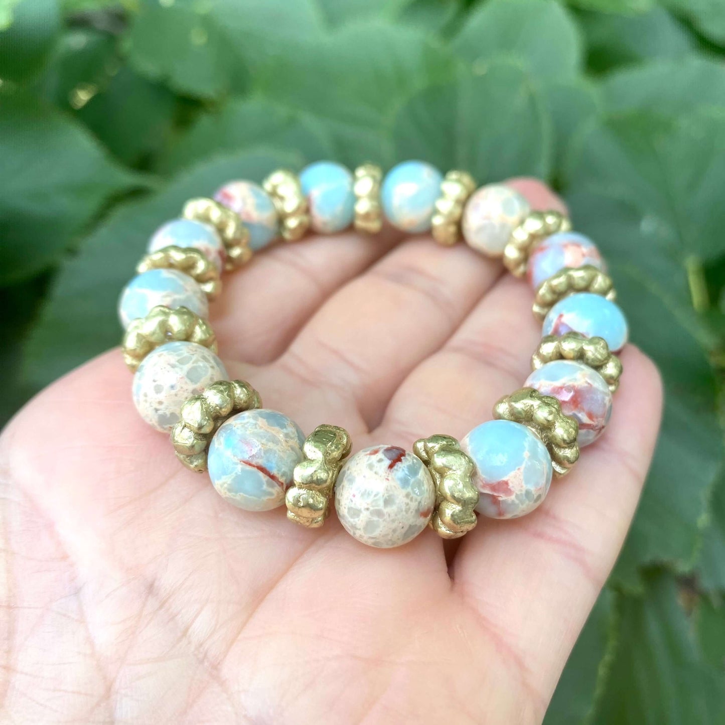 Pale blue deep red stretchy bracelet held in hand showing pale blue jasper and pearl details