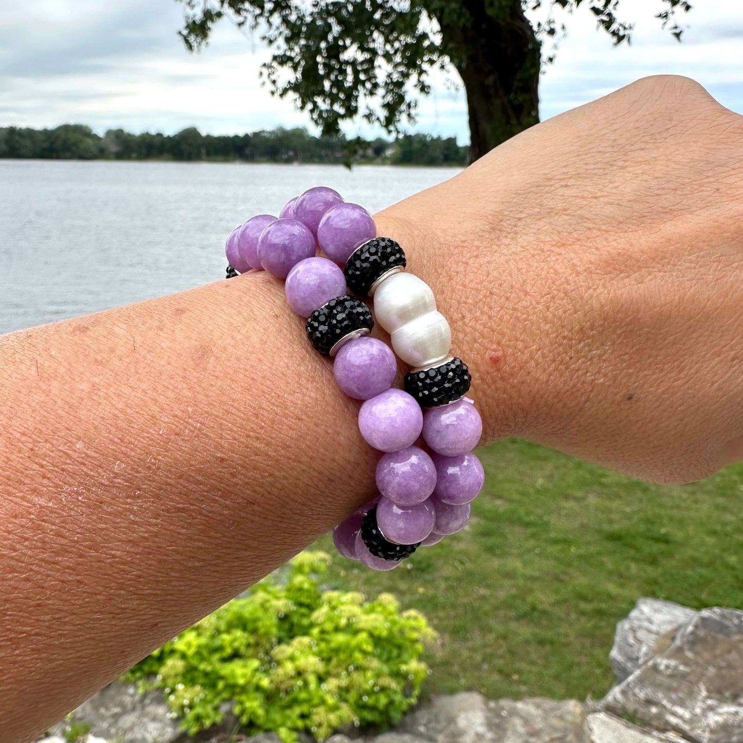 Two lavender jade bracelets worn together on a woman’s wrist near flowers