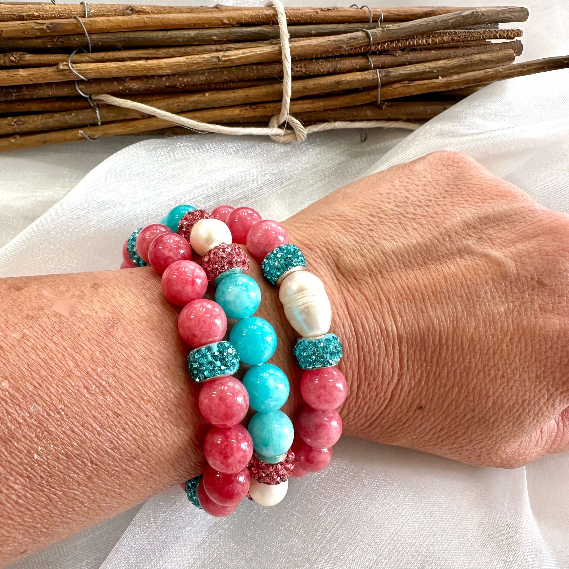 Teal jade bracelet with pearls and pink accents worn on a wrist, showcasing handmade jewelry craftsmanship.