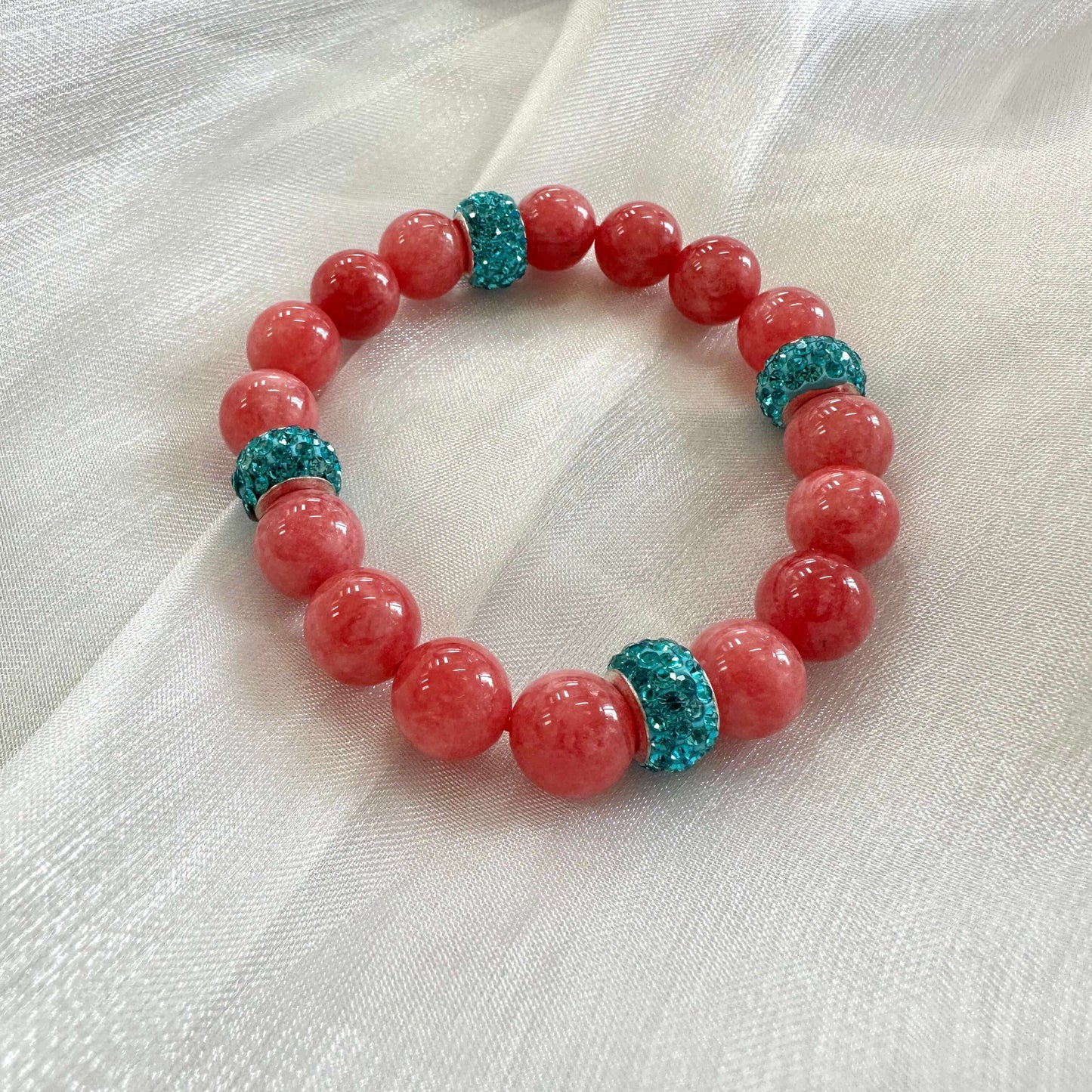 Red jade bracelet without pearl and blue rhinestones displayed on white cloth