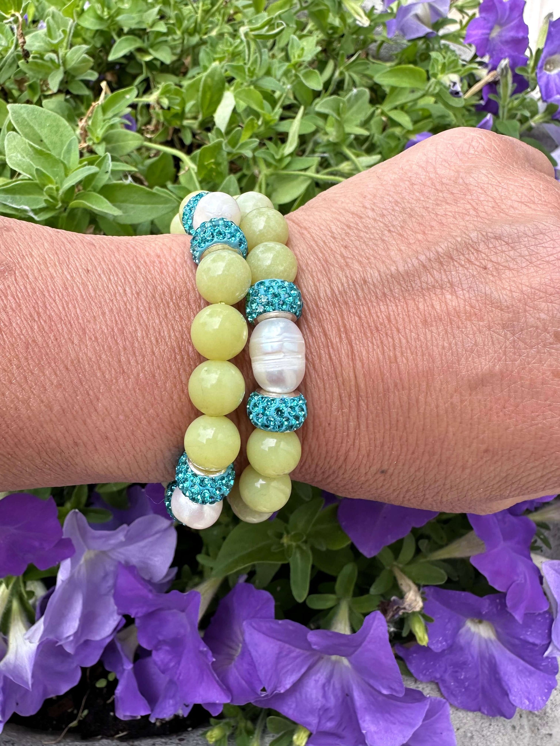 Two olive green jade bracelets with pearls worn on a woman’s wrist outdoors