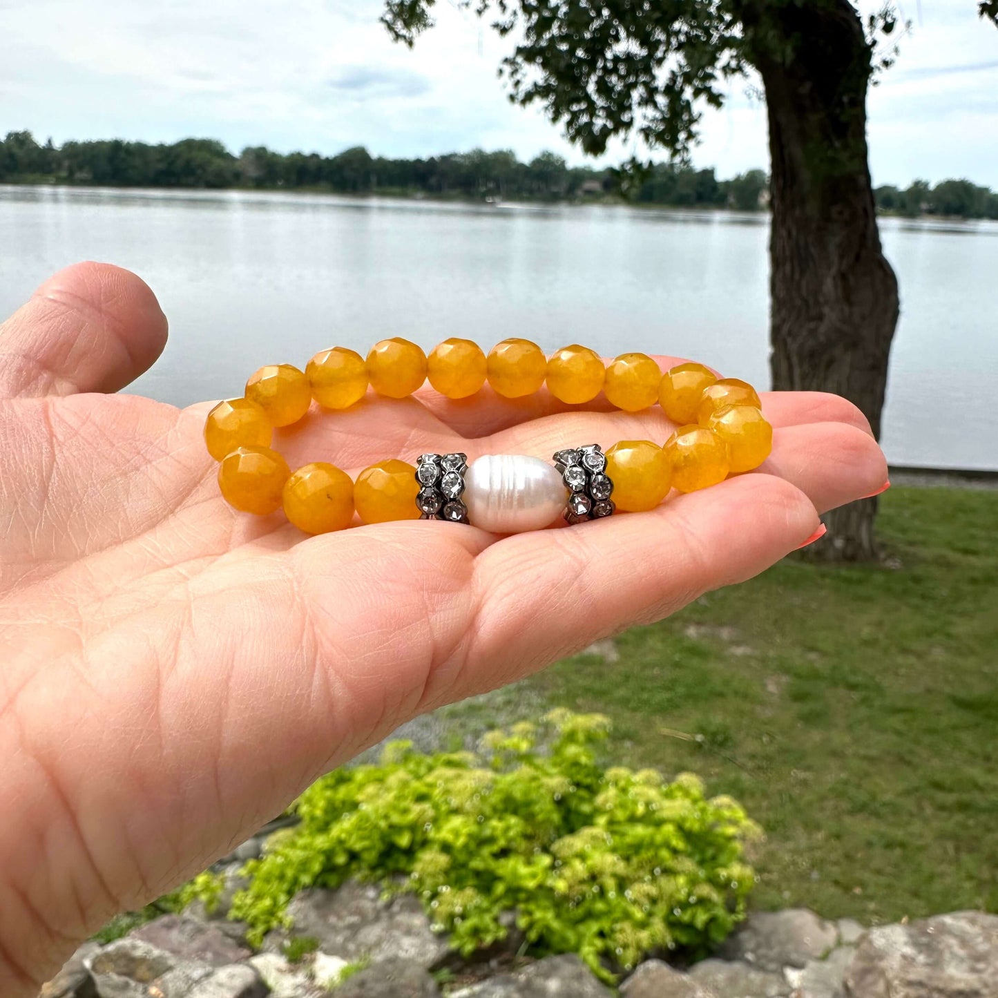 Yellow jade pearl bracelet held in hand near natural lake