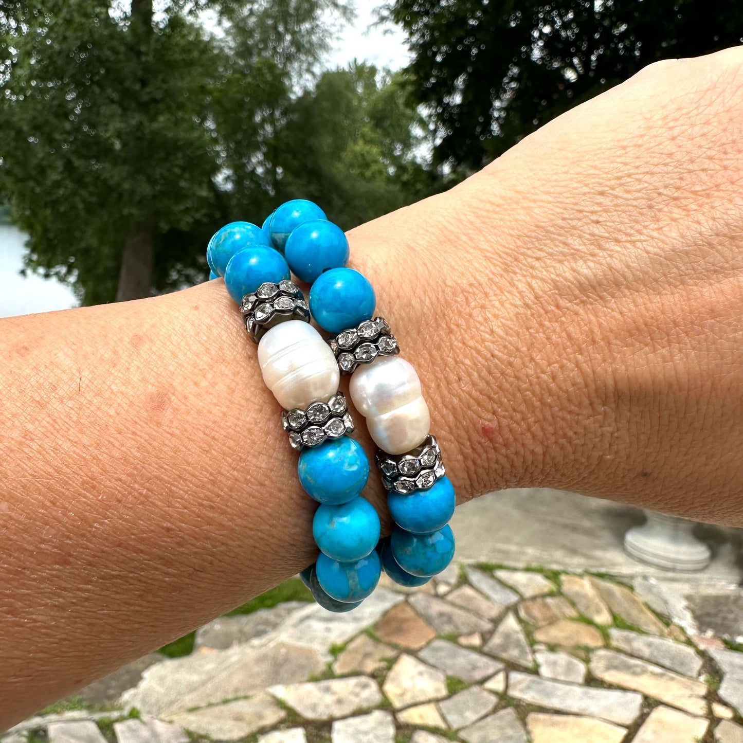 Two turquoise howlite pearl bracelets stacked on wrist near water in garden