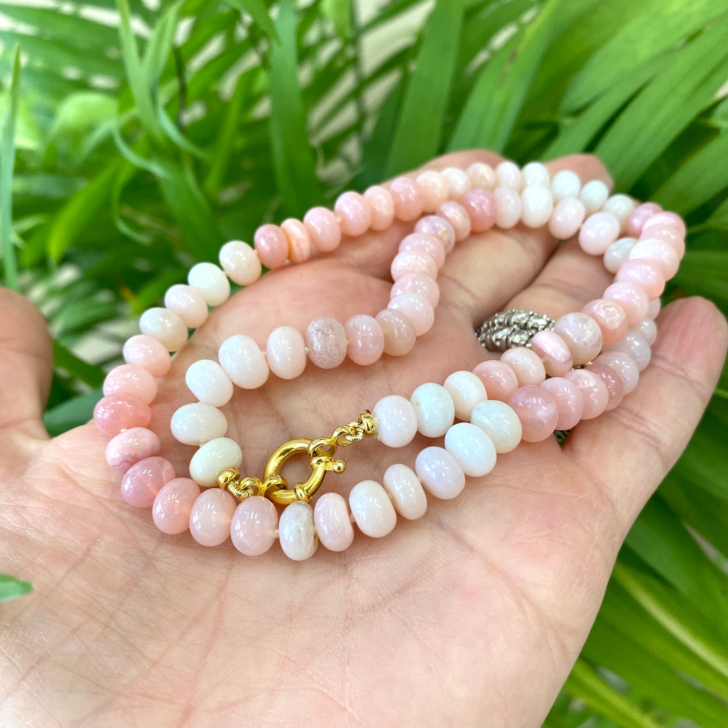 Pink opal beaded necklace held in hand against green leaves