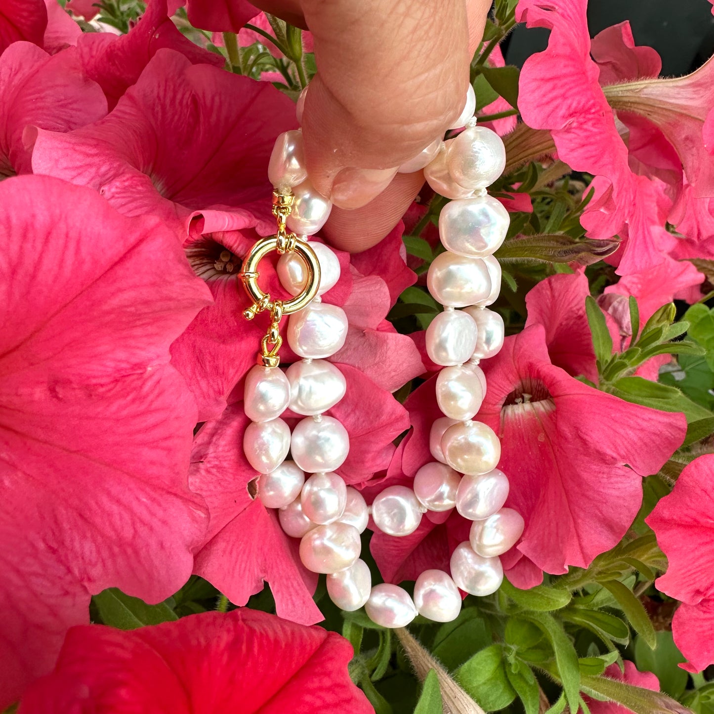 Hand holding a small baroque pearl classic necklace against vibrant pink flowers.