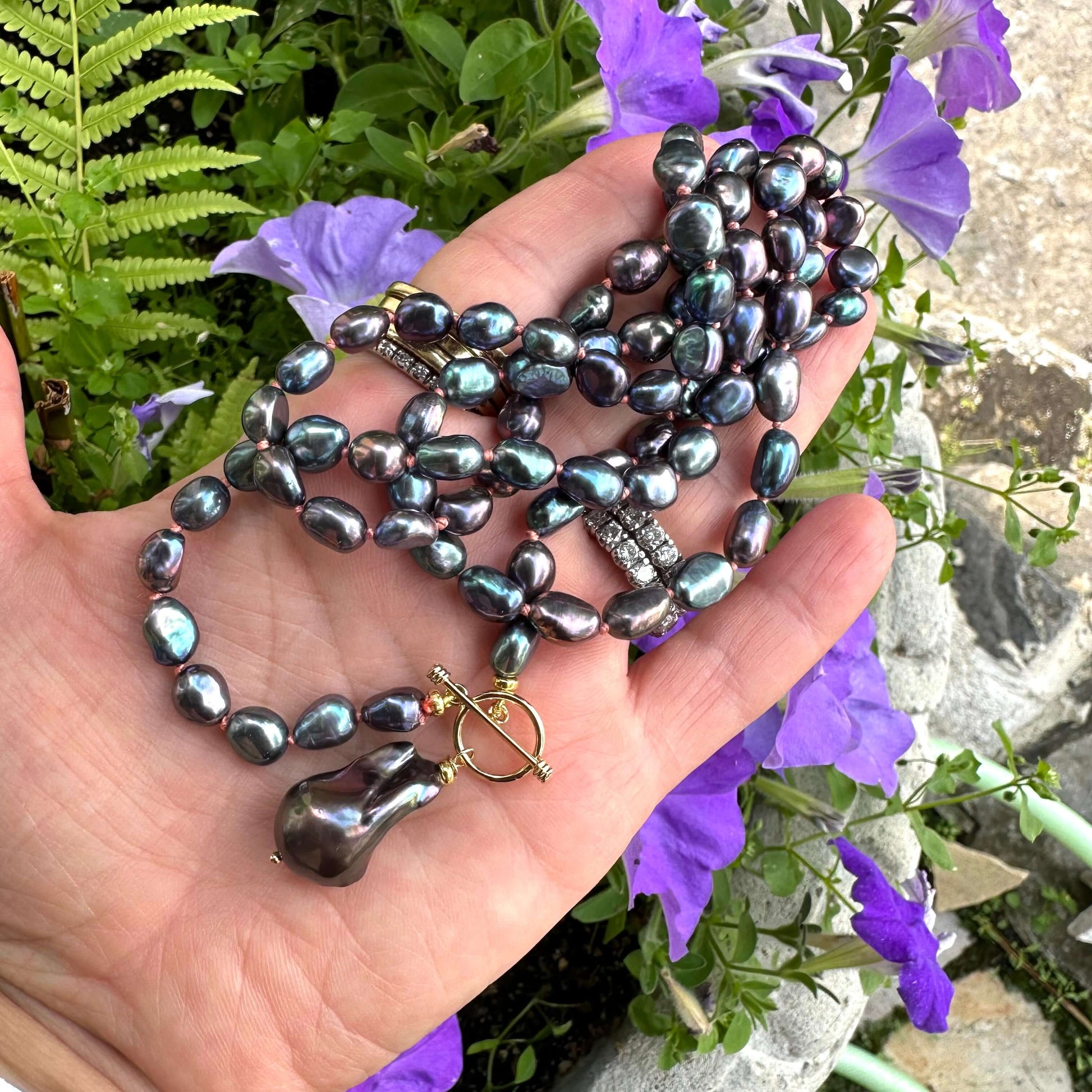 Peacock black pearl necklace with baroque pendant held in hand against flowers