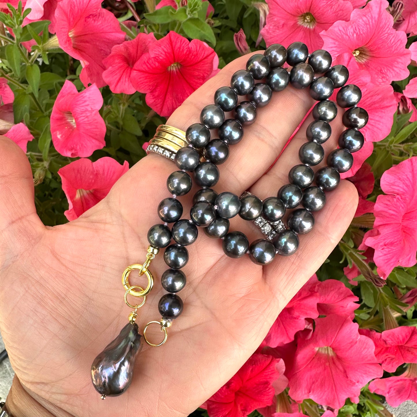 Black pearl necklace with baroque pendant held in hand near flowers