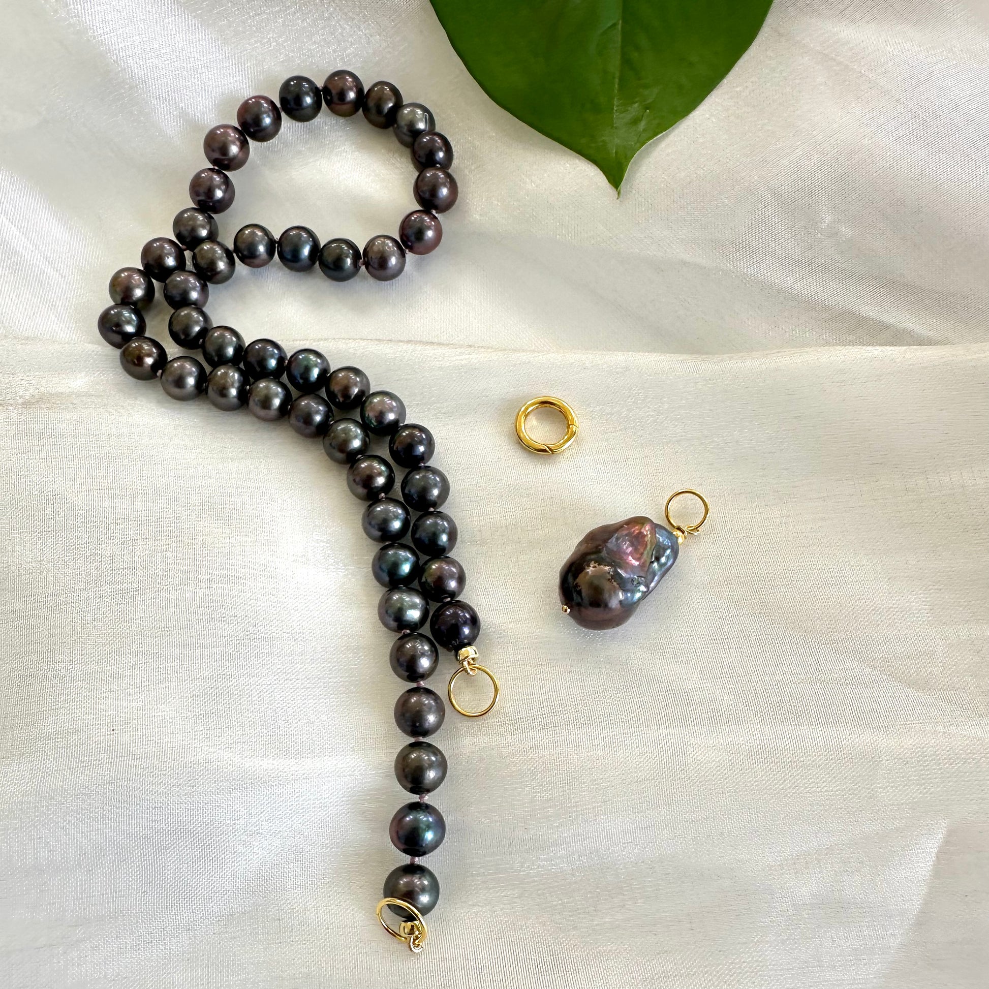 Black pearl necklace with baroque pendant shown next to removable pendant on white cloth