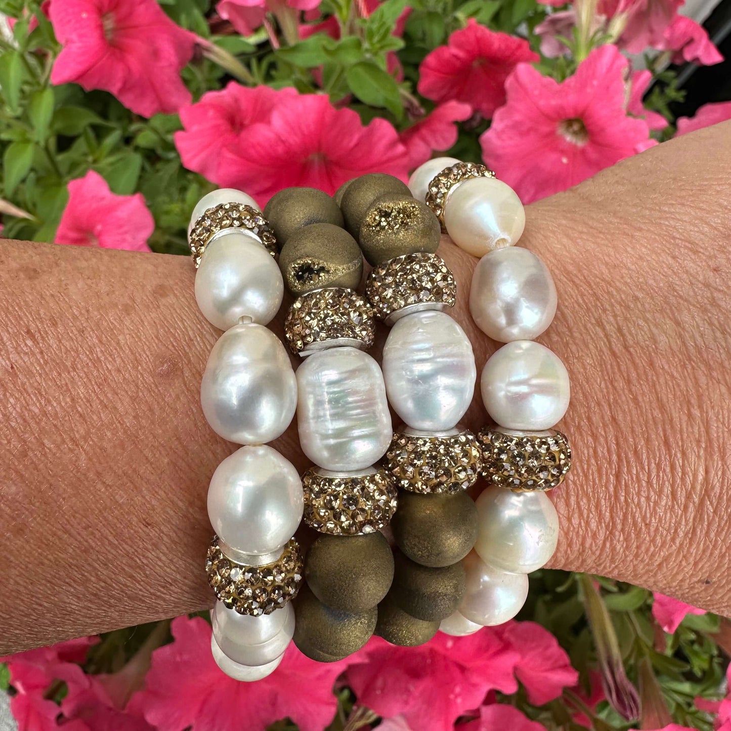 Stacked white pearl stretch bracelets with gold rhinestone accents on woman’s wrist outdoors