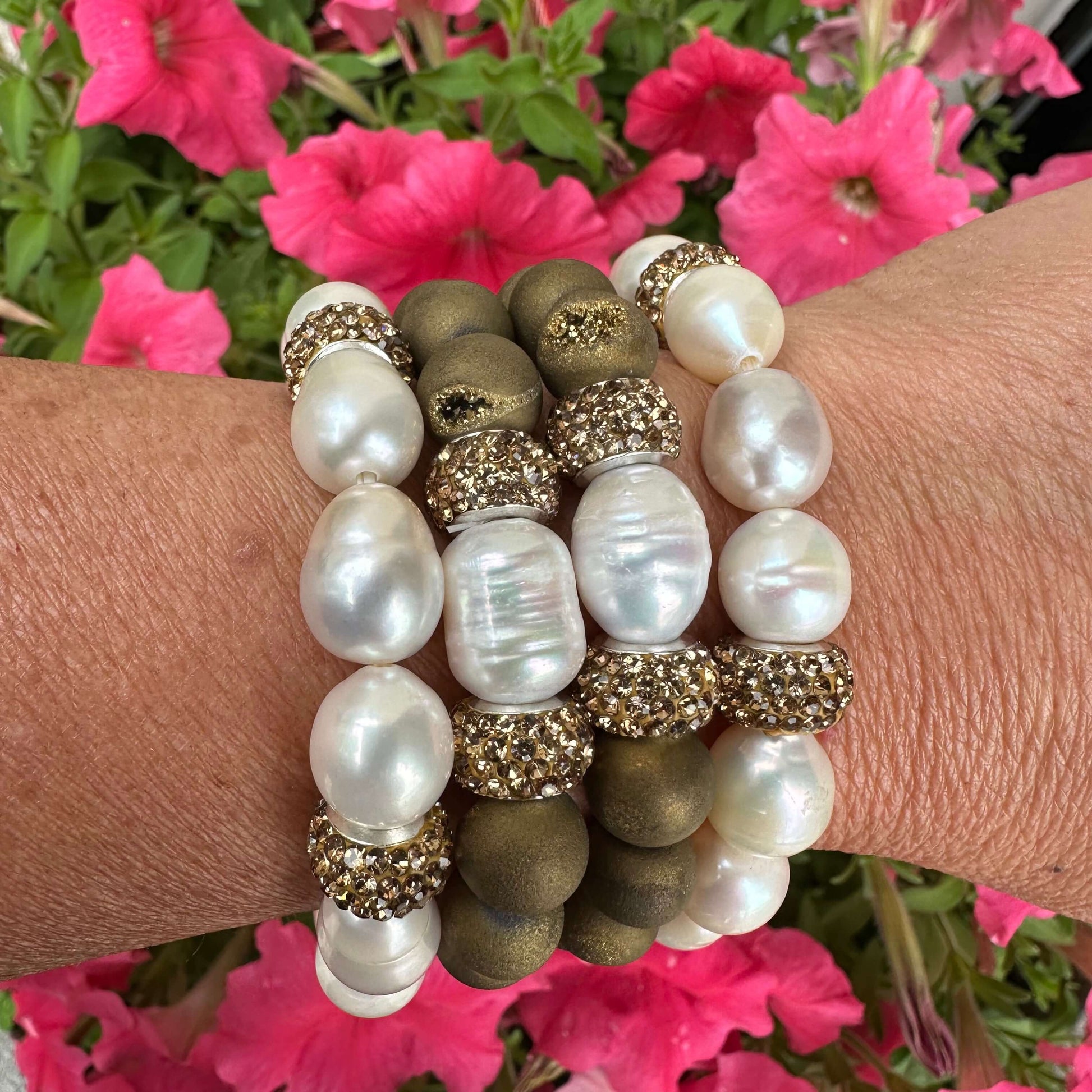 Stacked white pearl stretch bracelets with gold rhinestone accents on woman’s wrist outdoors
