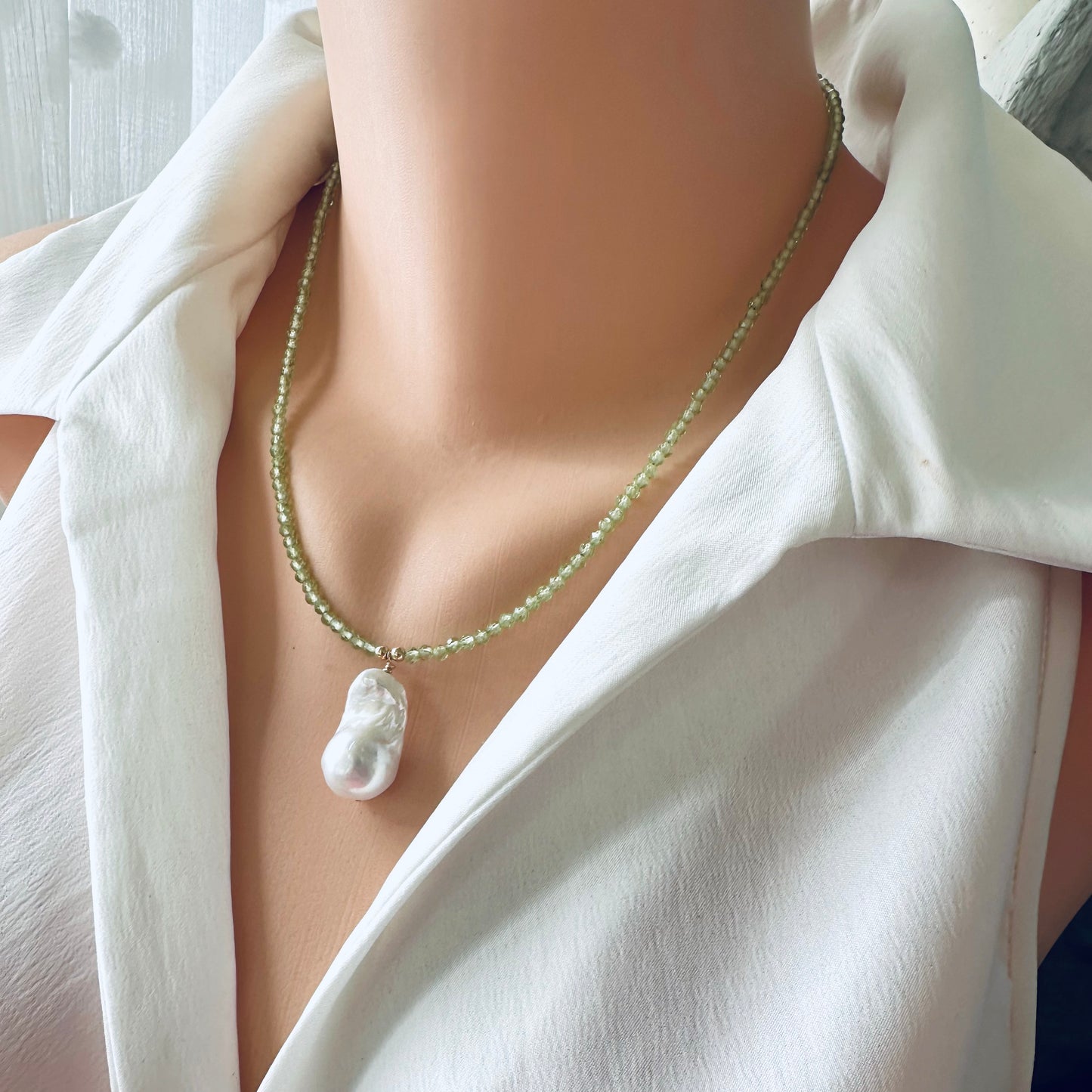 Peridot beaded necklace with baroque pearl pendant worn on mannequin, frontal close-up