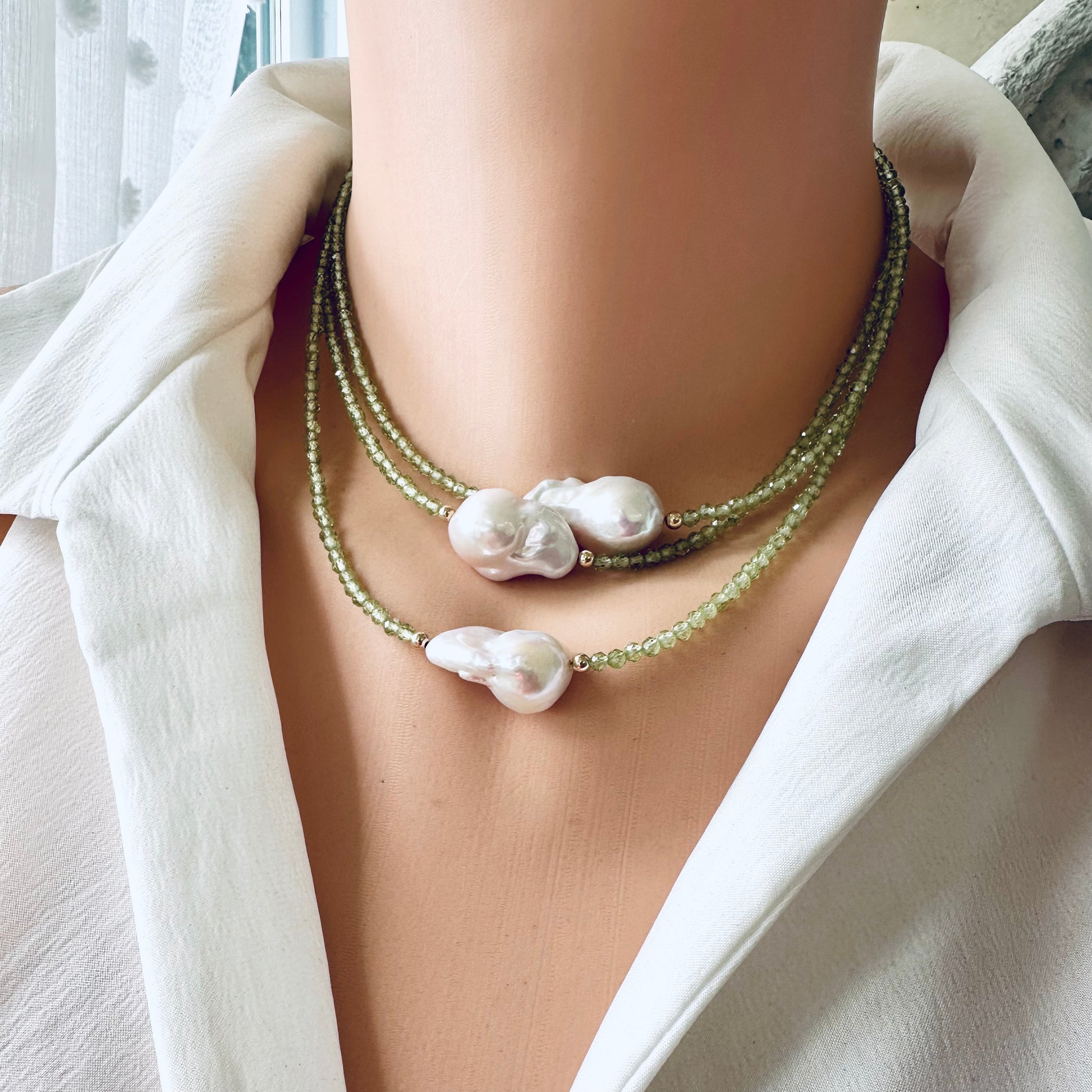 Two peridot and baroque pearl necklaces stacked on mannequin in frontal view