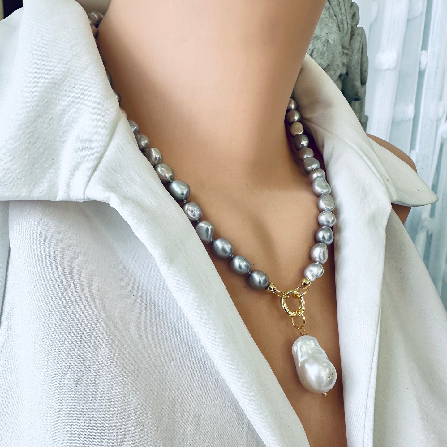 Grey pearl necklace with white baroque pearl pendant displayed on a mannequin wearing a white blouse.
