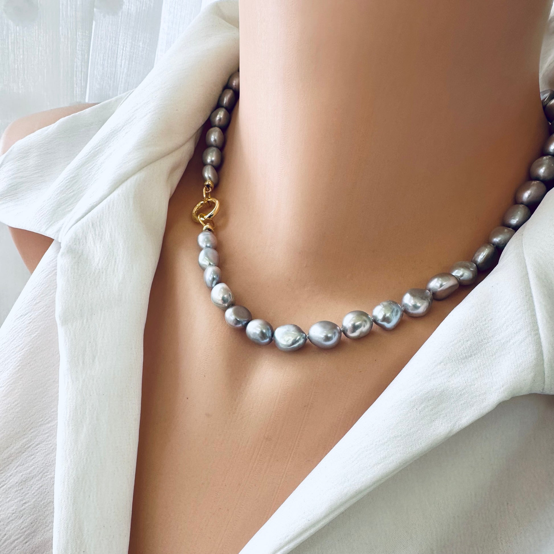 Grey pearl necklace with silver-grey freshwater pearls and gold clasp worn on a mannequin's neck.
