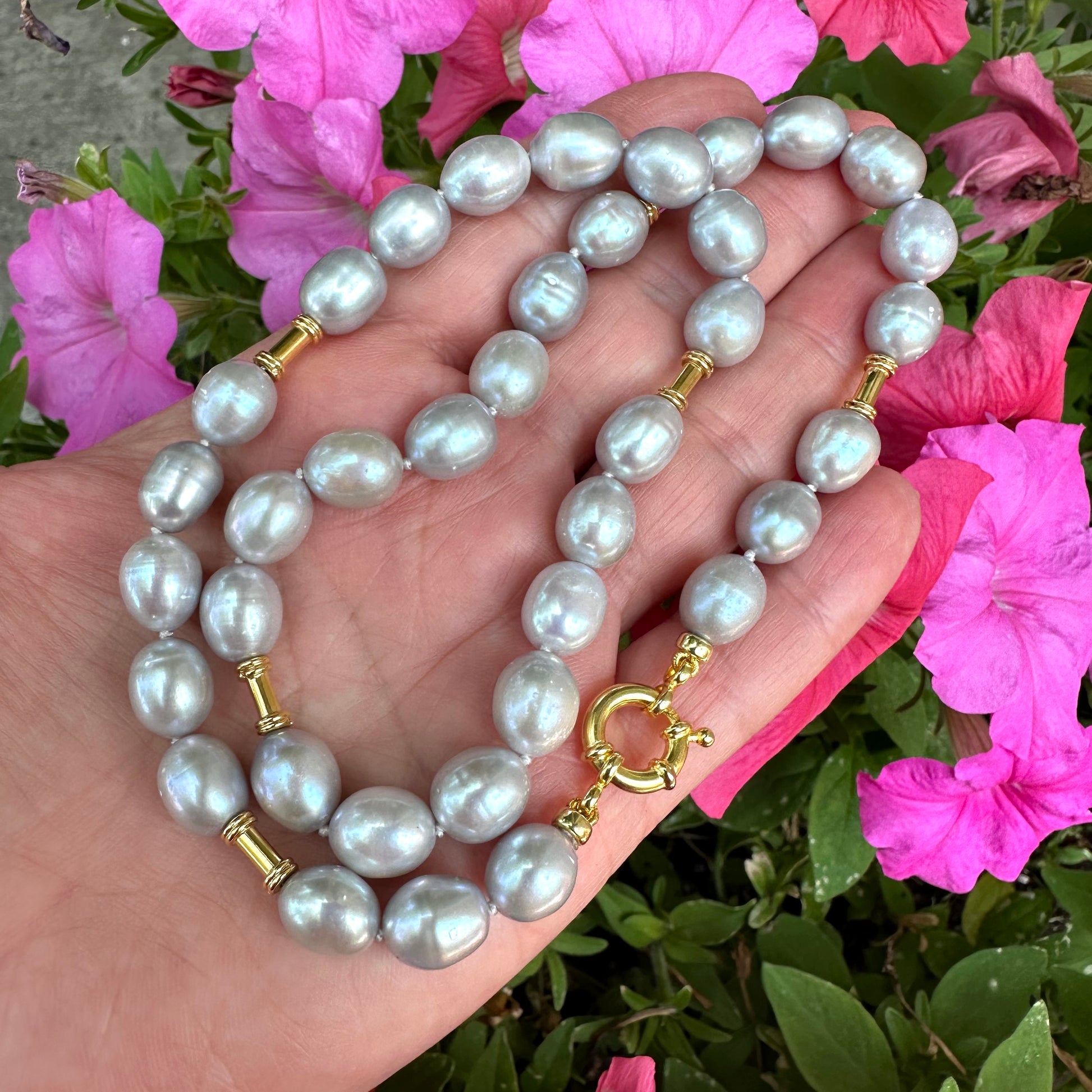 Grey pearl necklace with gold details held in hand against pink flowers