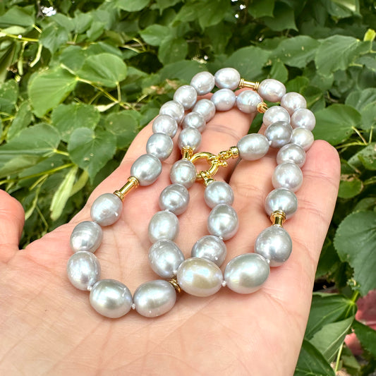Grey pearl necklace with gold details held in hand against green foliage