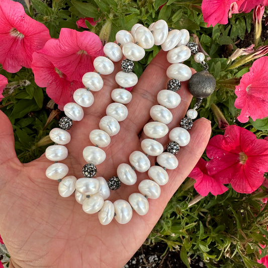 Close-up of white button pearl necklace with rhinestone pave beads held outdoors near foliage
