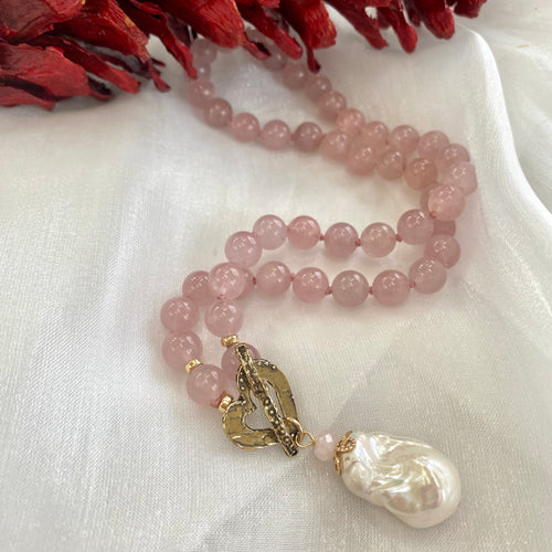 Smooth 8mm hand knotted rose quartz round bead necklace with a baroque pearl pendant, featuring an artisan gold bronze heart toggle clasp and gold-filled details. The necklace is 17.5 inches long and makes a thoughtful January birthstone gift