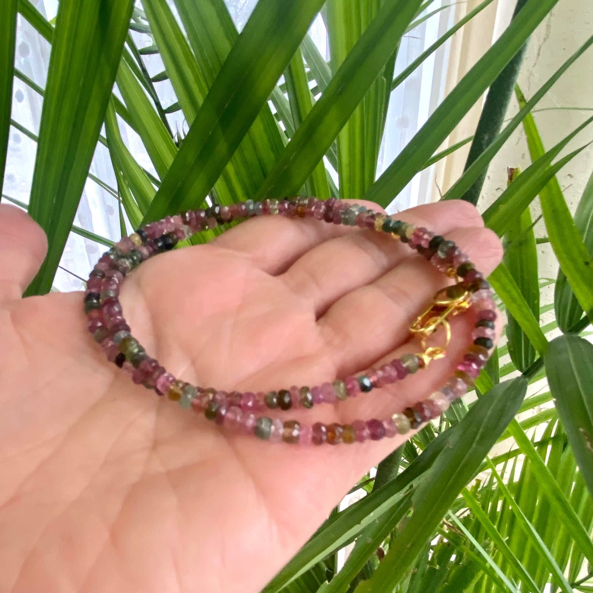 Watermelon tourmaline necklace held in hand against green leaves