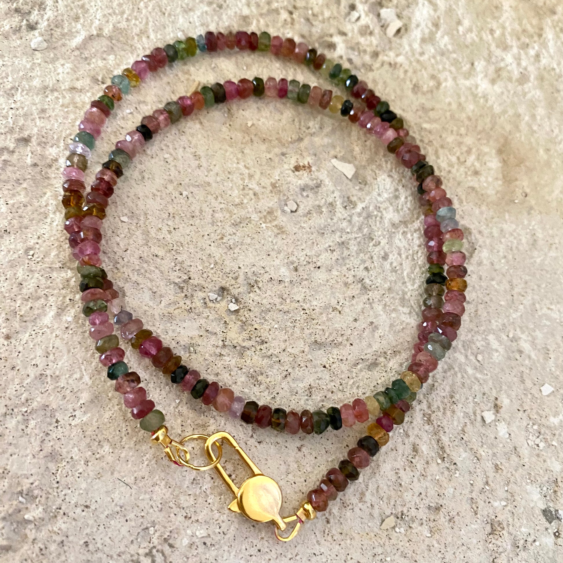 Watermelon tourmaline necklace displayed on beige stone surface