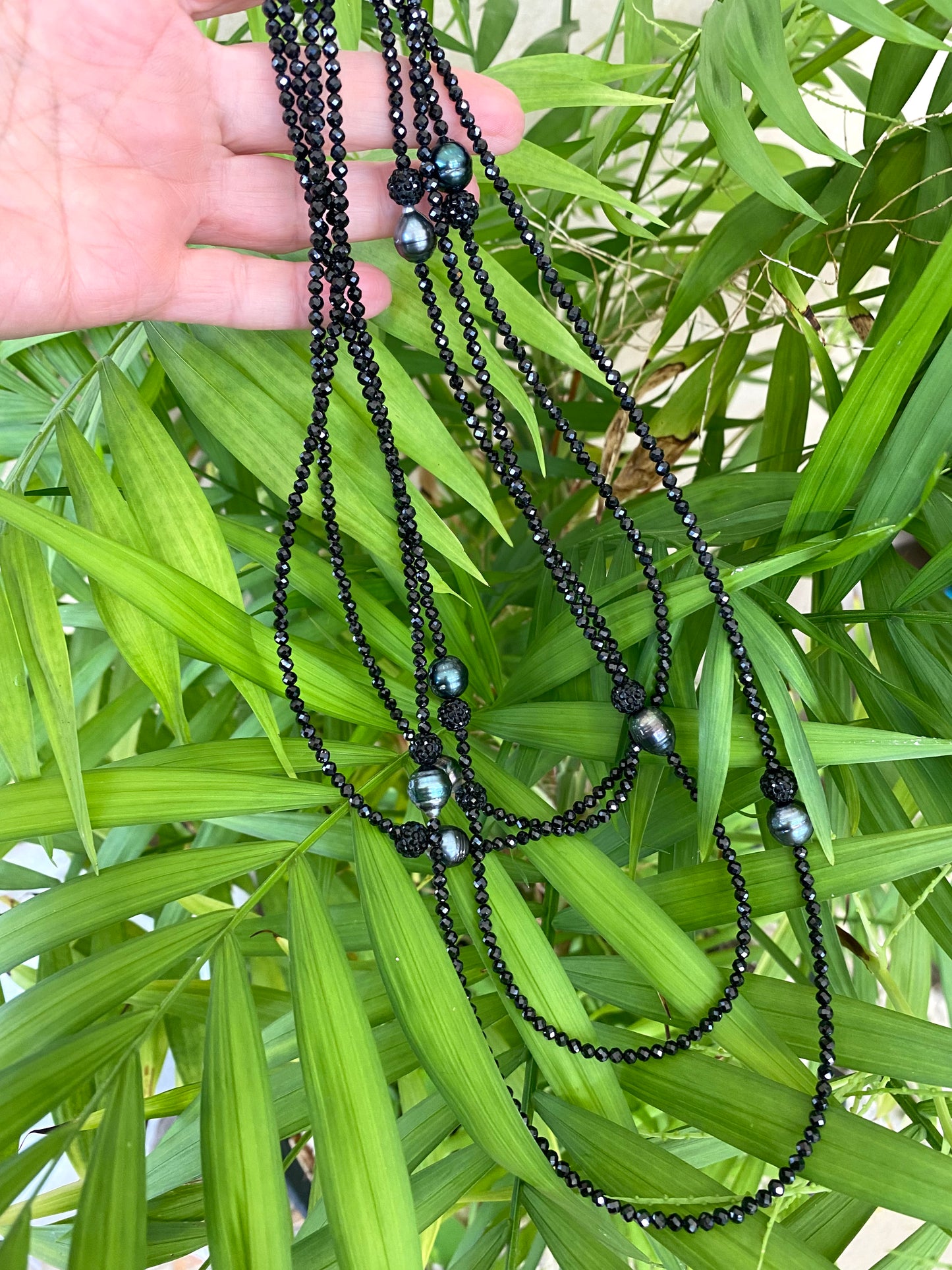 Black spinel pearl necklace held against green leaves