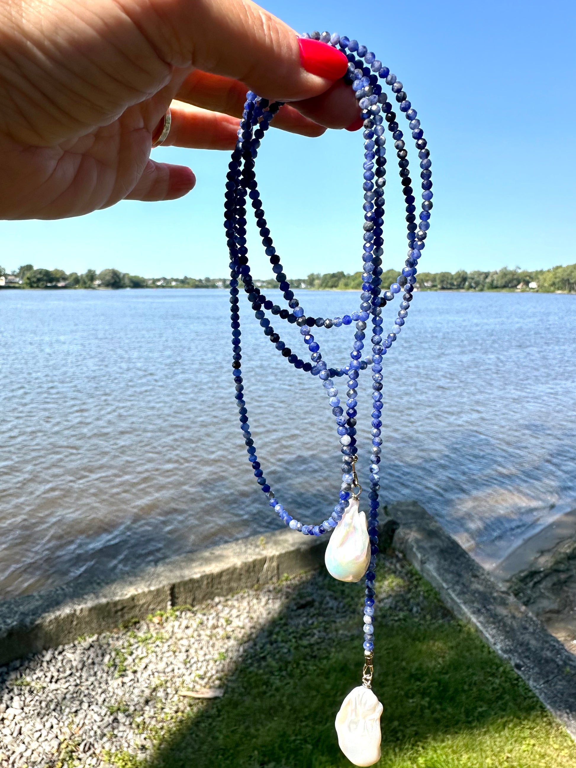 Sodalite baroque pearl lariat necklace held outdoors showing length and pearl drops