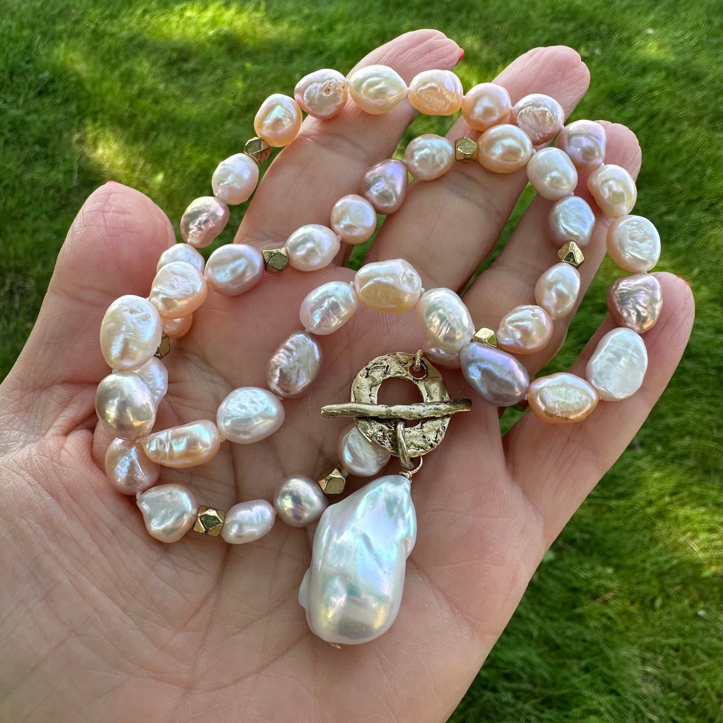 Pastel pearl necklace displayed outdoors against green leaves and lake background, natural light