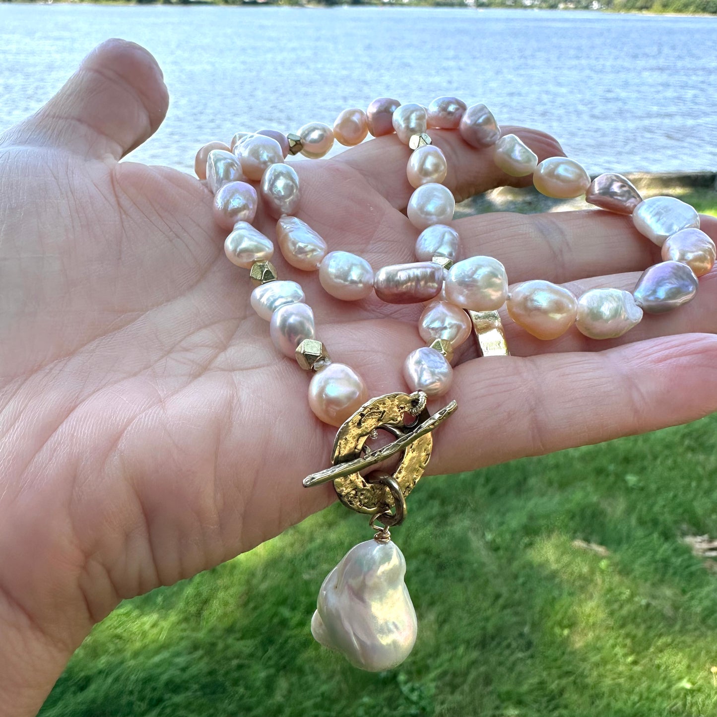 Pastel pearl necklace held in hand near water reflecting soft pastel pearl colors
