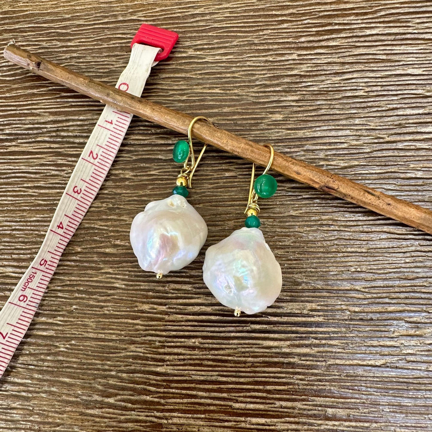 White baroque pearl drop earrings with green agate and gold accents on a wooden background