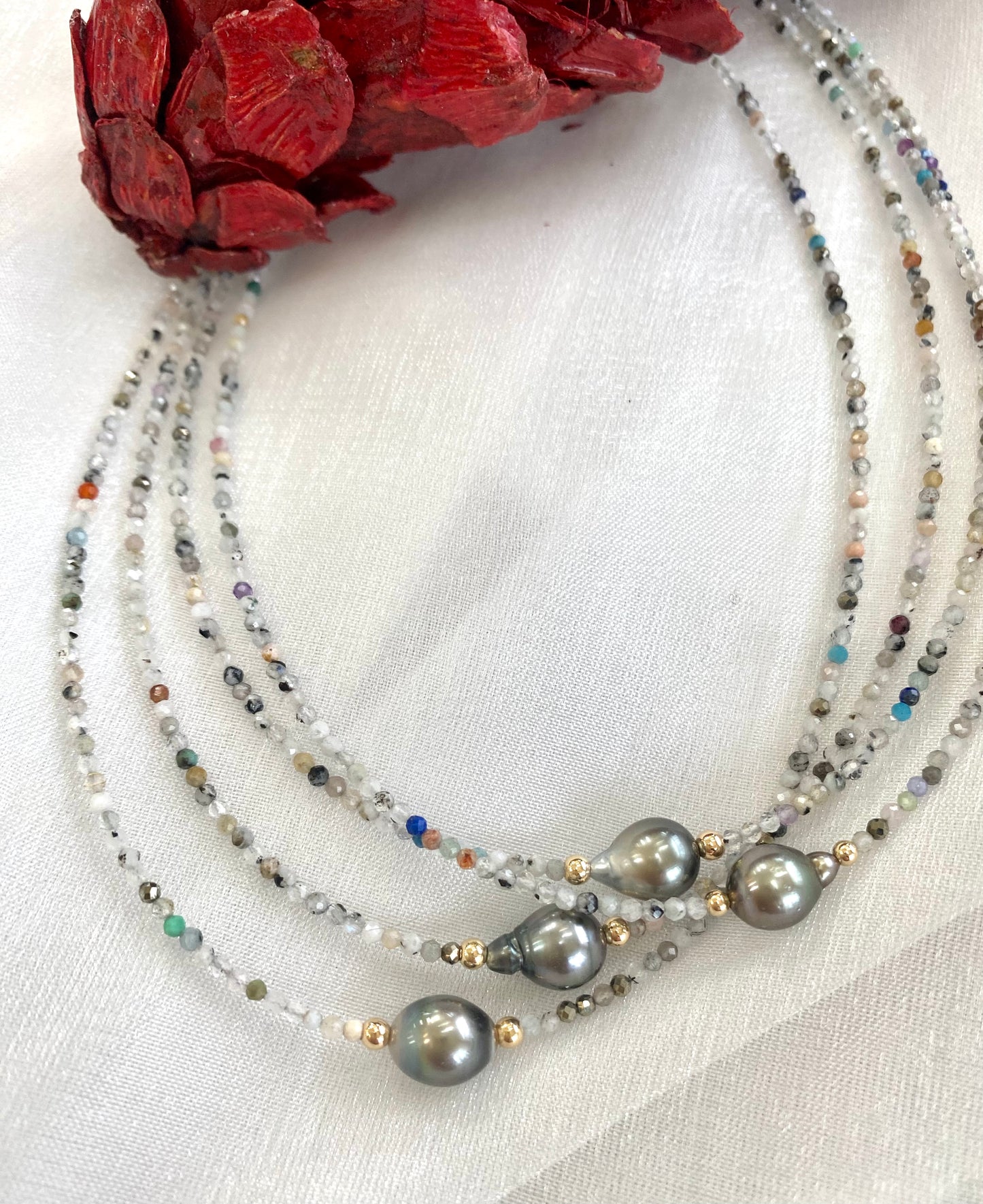 Multi stone pearl necklace displayed in different color variations on white cloth