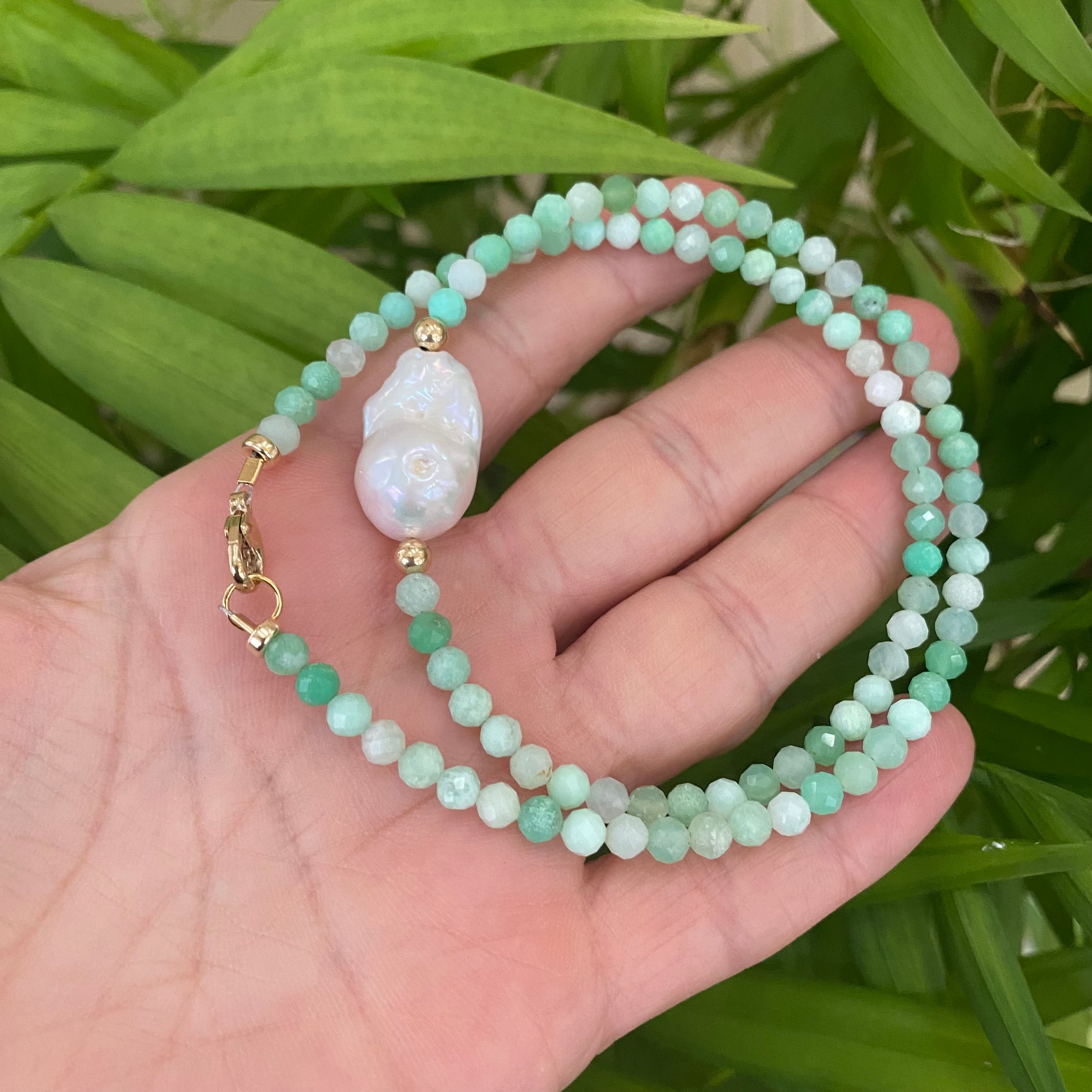 Chrysoprase pearl necklace held in hand against green leaves