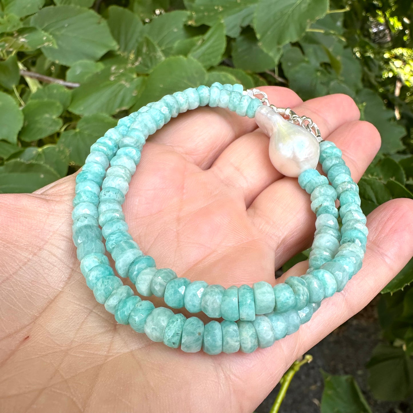Close-up of amazonite and white baroque pearl necklace held in hand showing gemstone color variations