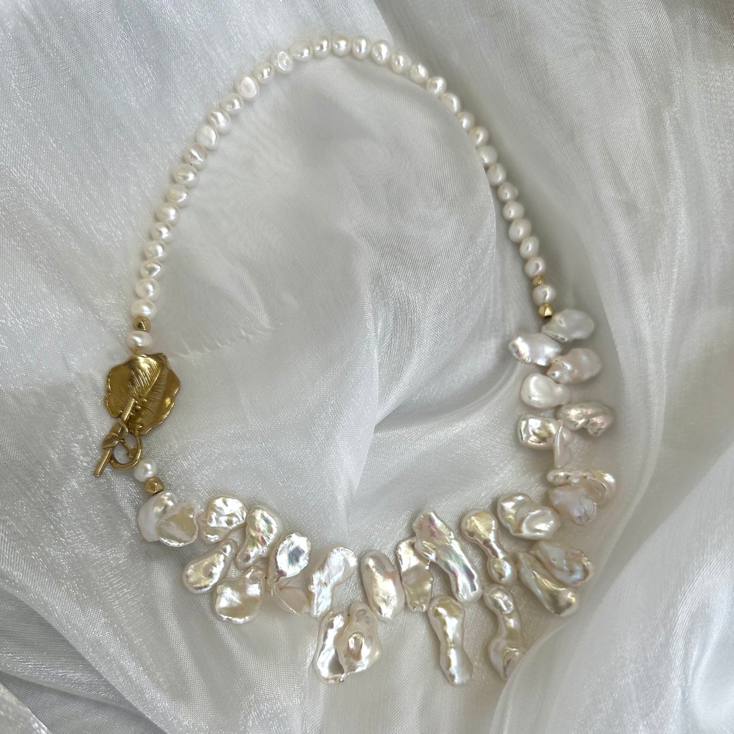 Close-up of white petal pearl necklace on white fabric highlighting asymmetrical pearls