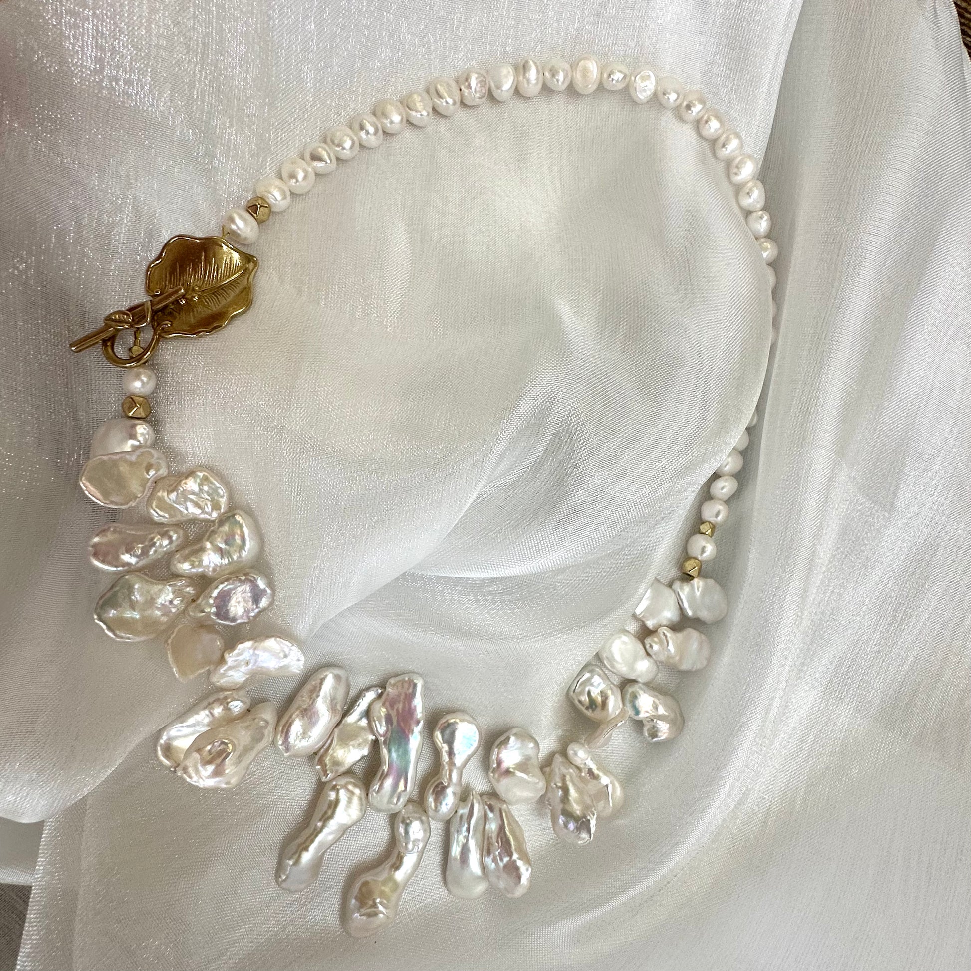 White petal pearl necklace displayed on white cloth background showing golden leaf clasp