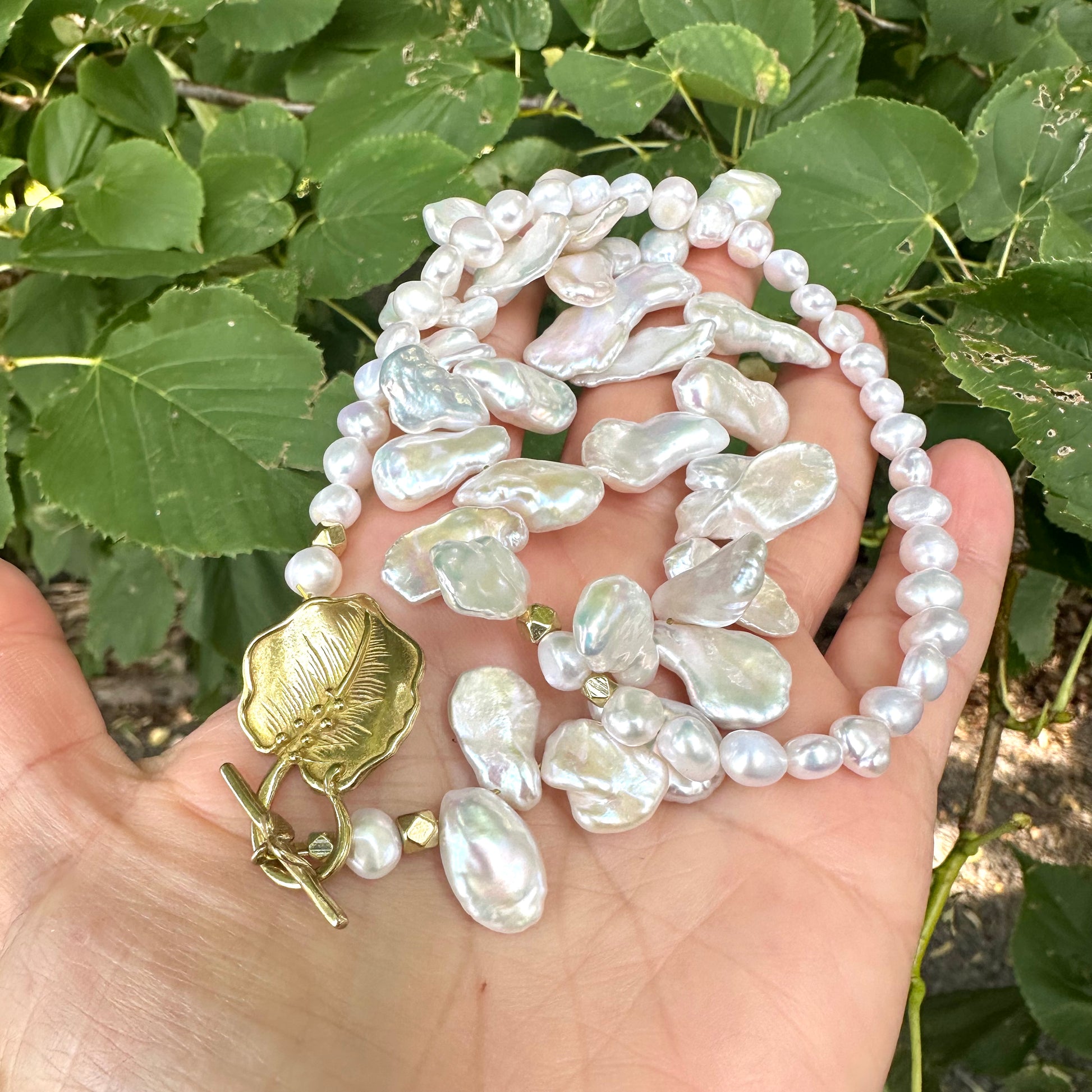 White petal pearl necklace held in hand with green foliage background under daylight
