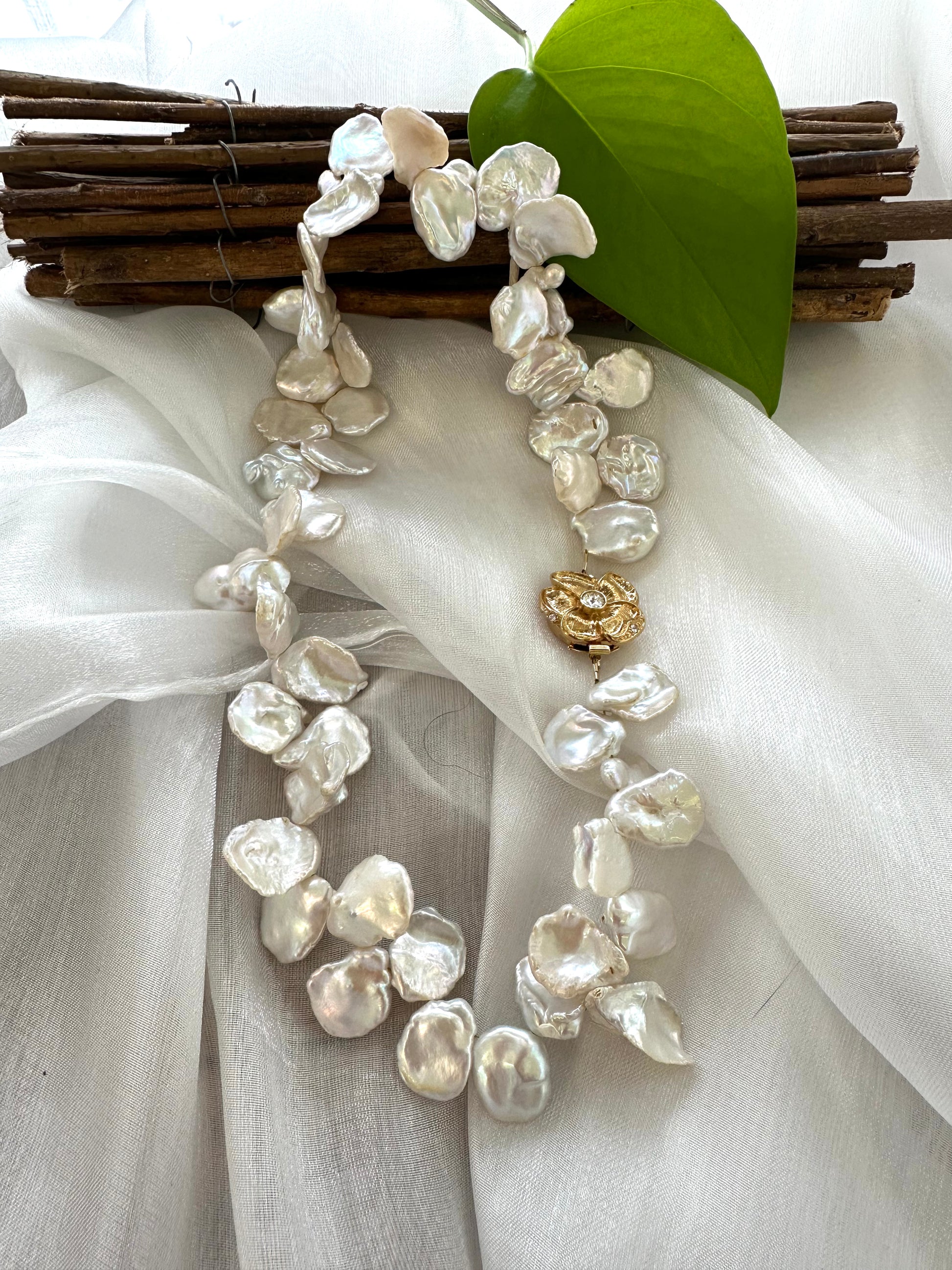 White keshi pearl necklace with flower clasp displayed on white cloth table, detailed view of pearls