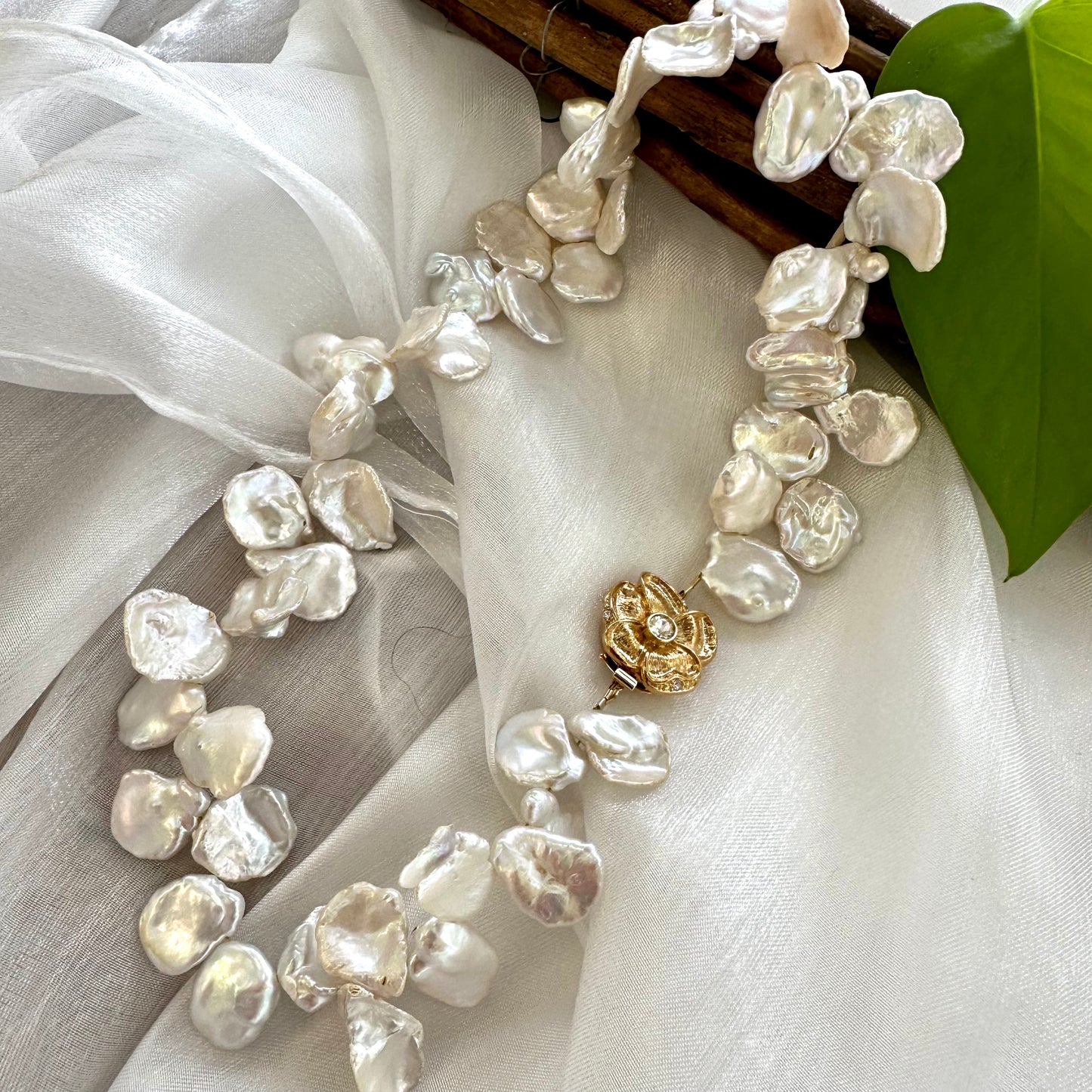 White keshi pearl necklace with flower clasp arranged on white cloth for product photography