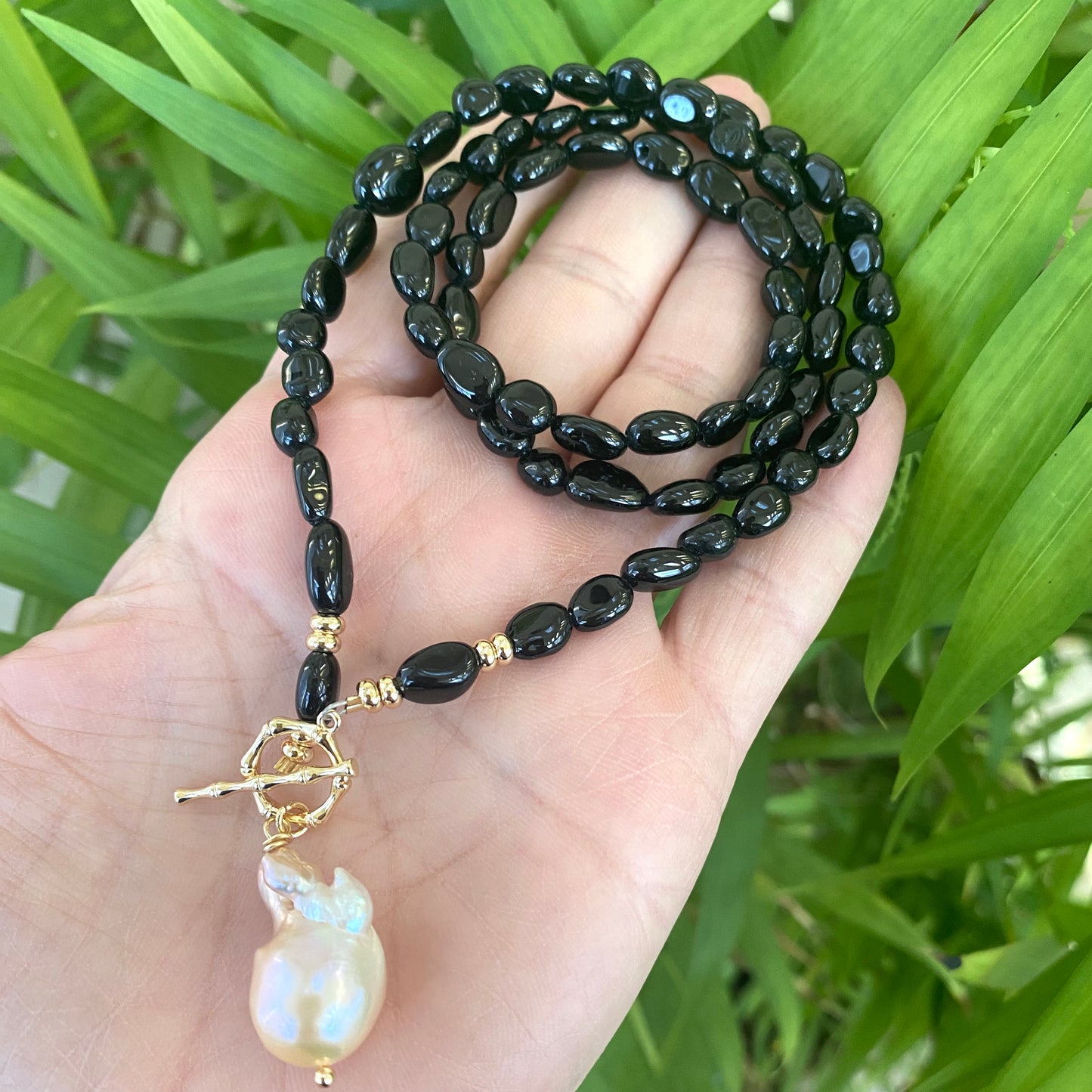 Black tourmaline pearl necklace held in hand against green foliage