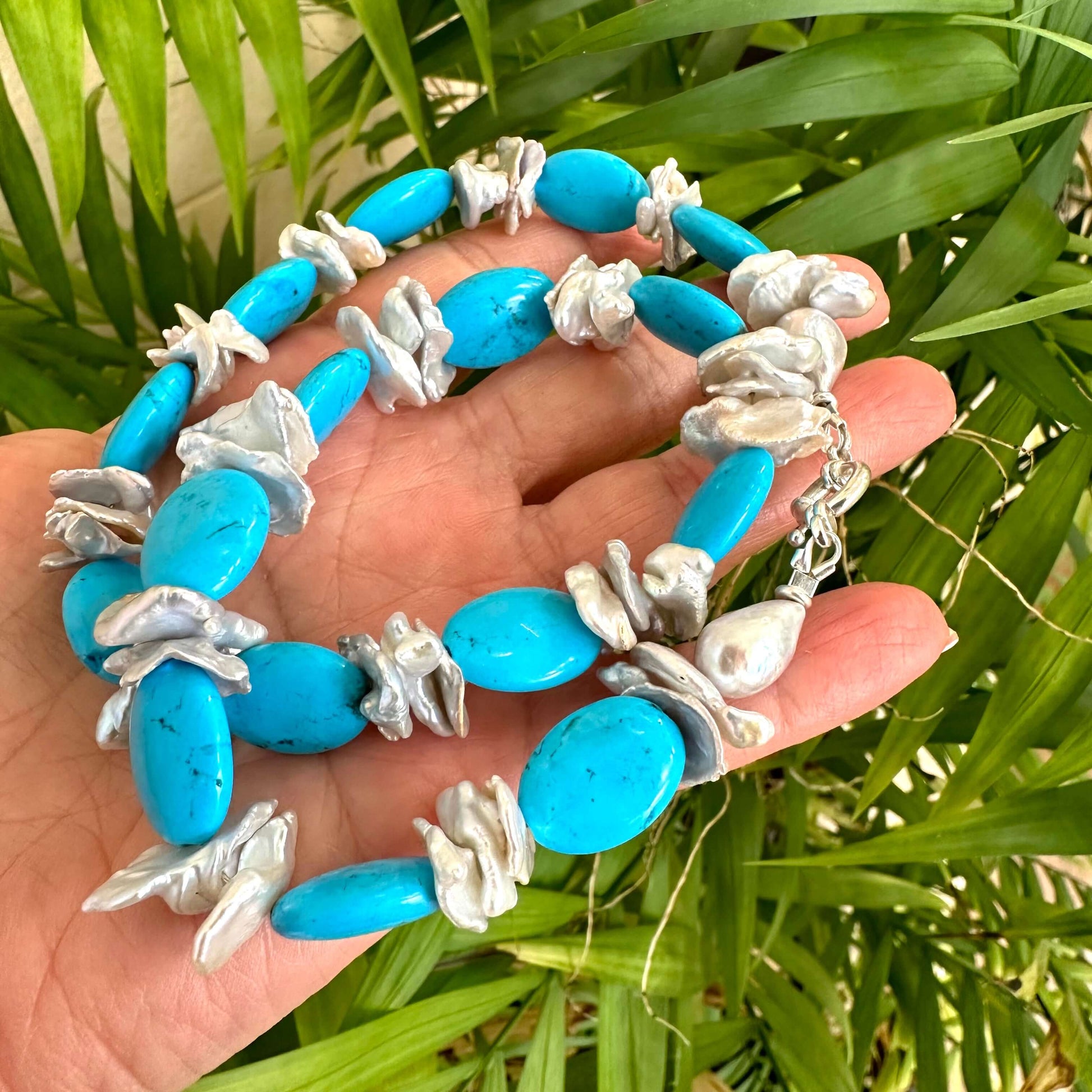 Chunky turquoise and silver grey keshi pearl necklace held in hand against green foliage backdrop