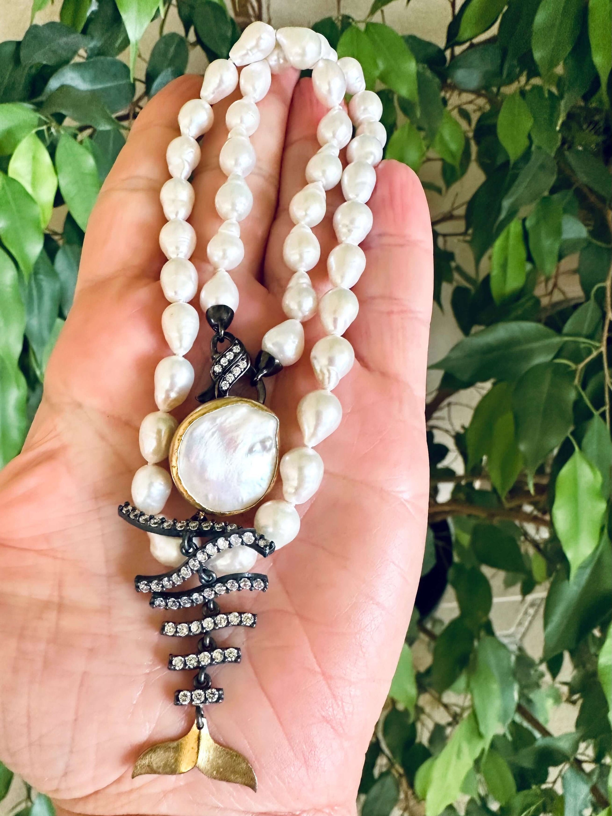 Small baroque pearl necklace held in hand against green foliage handmade in Canada